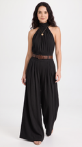 A woman modeling a black halter-neck wide-leg jumpsuit with a brown belt, photographed against a plain light gray studio background, from Meleche Fashion USA or Meléche (short as (Mé))