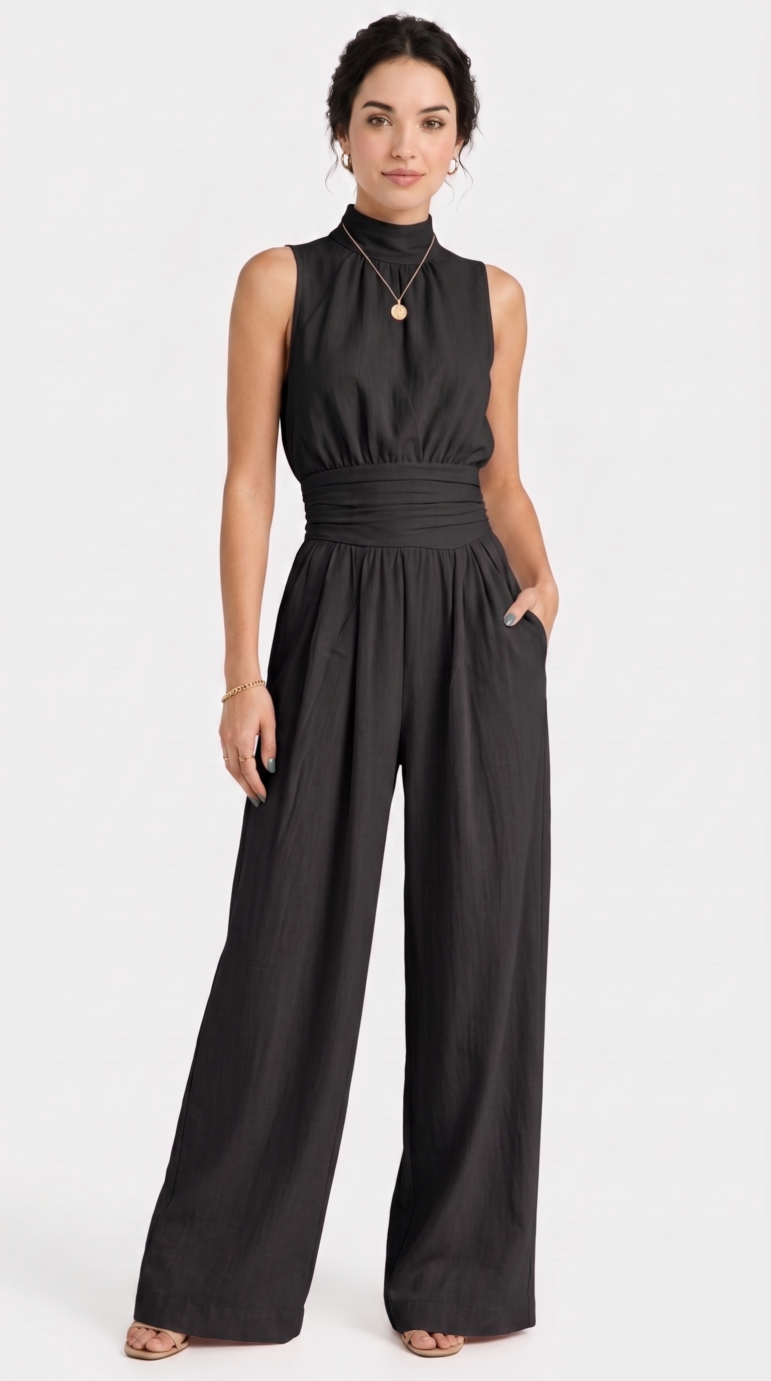 A woman modeling a black sleeveless high-neck jumpsuit with a gathered waist and wide legs, photographed against a plain light gray studio background, from Meleche Fashion USA or Meléche (short as (Mé))
