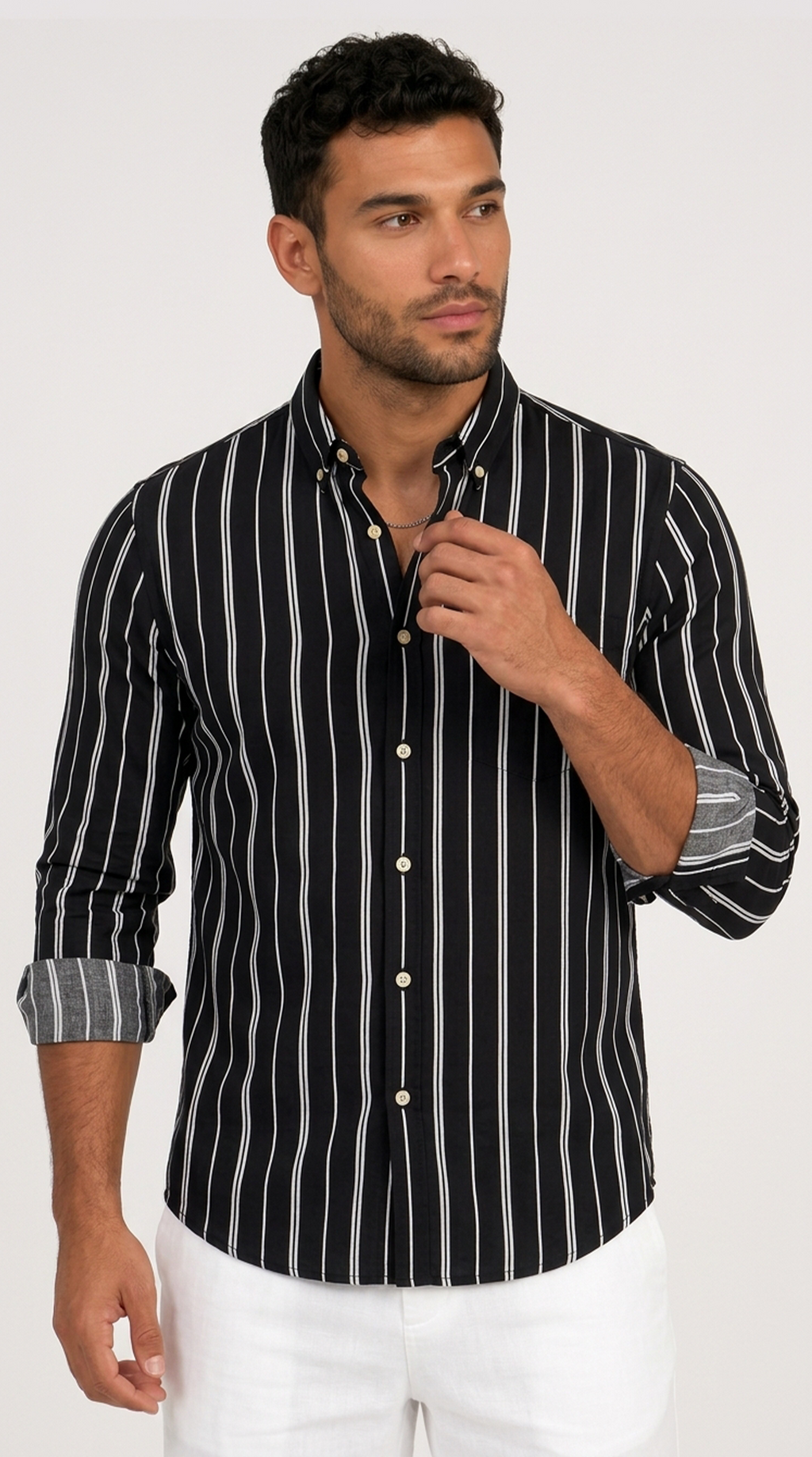 A man wearing a black long-sleeve button-down shirt with vertical white stripes and white pants, standing against a light gray studio background, from Meleche Fashion USA or Meléche (short as (Mé))