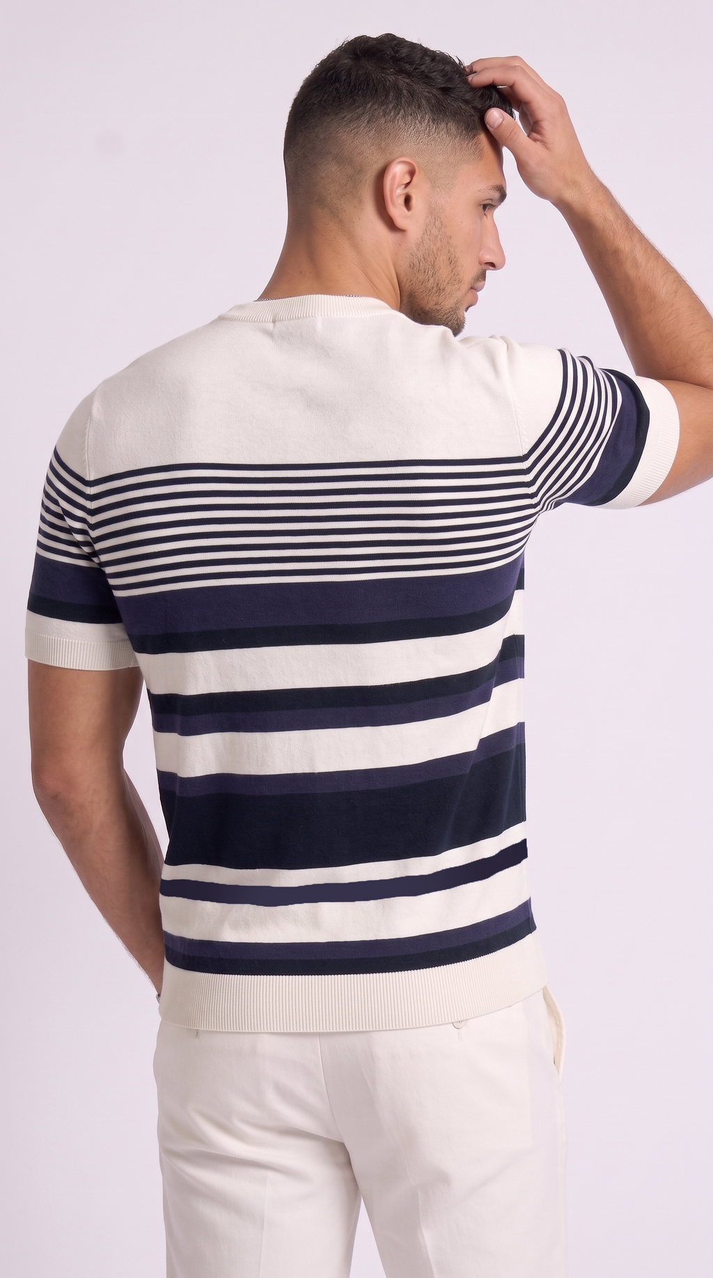 A man shown from the back wearing a short-sleeve knit sweater with horizontal navy and off-white stripes, paired with off-white trousers, against a light studio background, from Meleche Fashion USA or Meléche (short as (Mé))