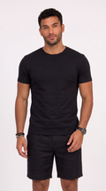 A man wearing a black short-sleeve crewneck t-shirt and black shorts, standing against a plain white studio background, from Meleche Fashion USA or Meléche (short as (Mé))