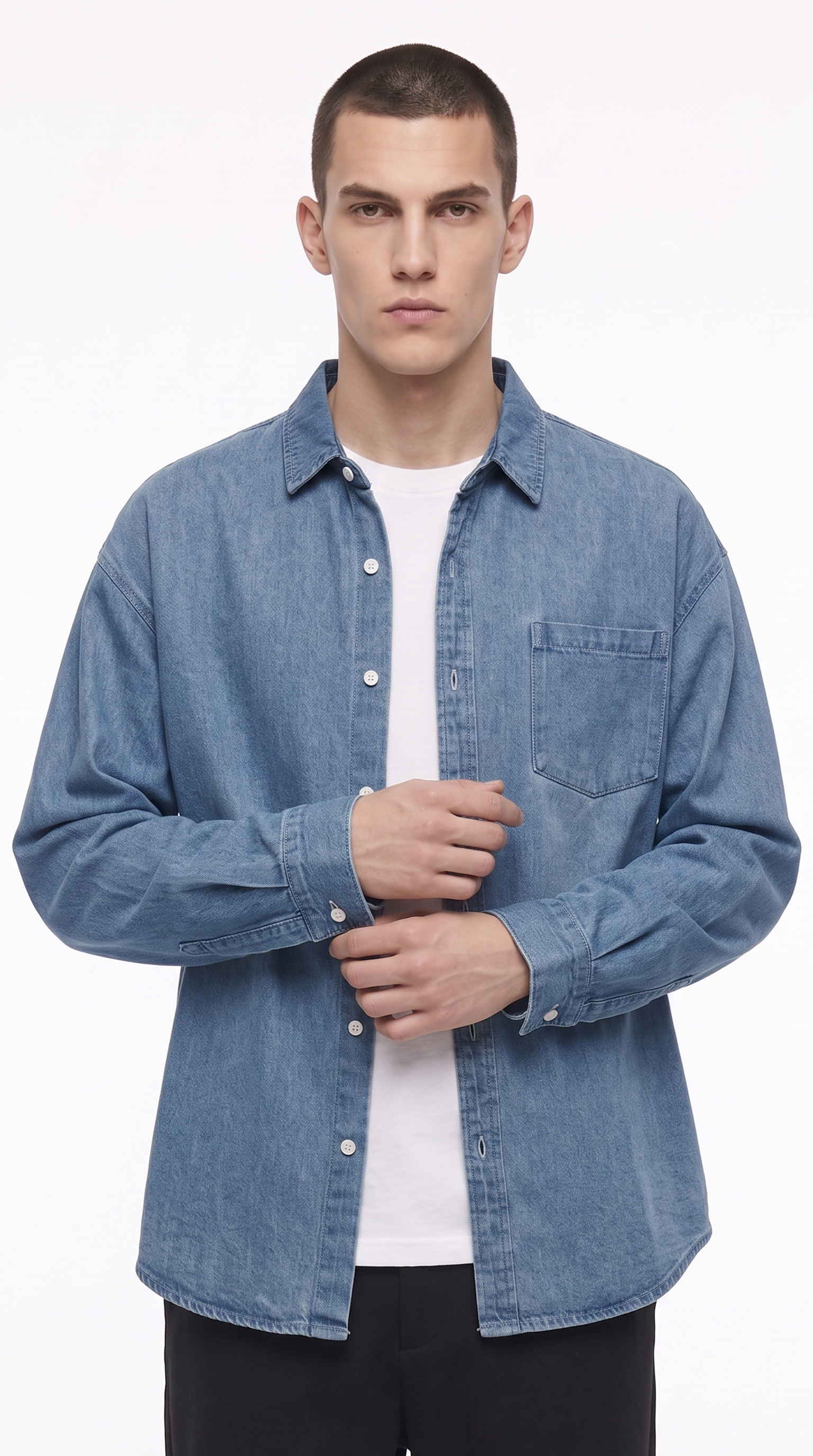 A man wearing a light blue denim button-up shirt over a white t-shirt and black pants, photographed against a plain white studio background, from Meleche Fashion USA or Meléche (short as (Mé))