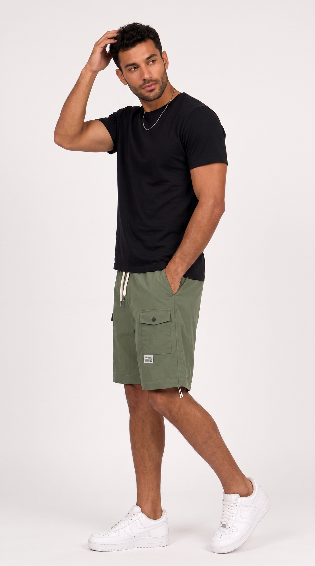 A man modeling olive green cargo shorts with a black t-shirt and white sneakers against a plain white studio background, from Meleche Fashion USA or Meléche (short as (Mé))