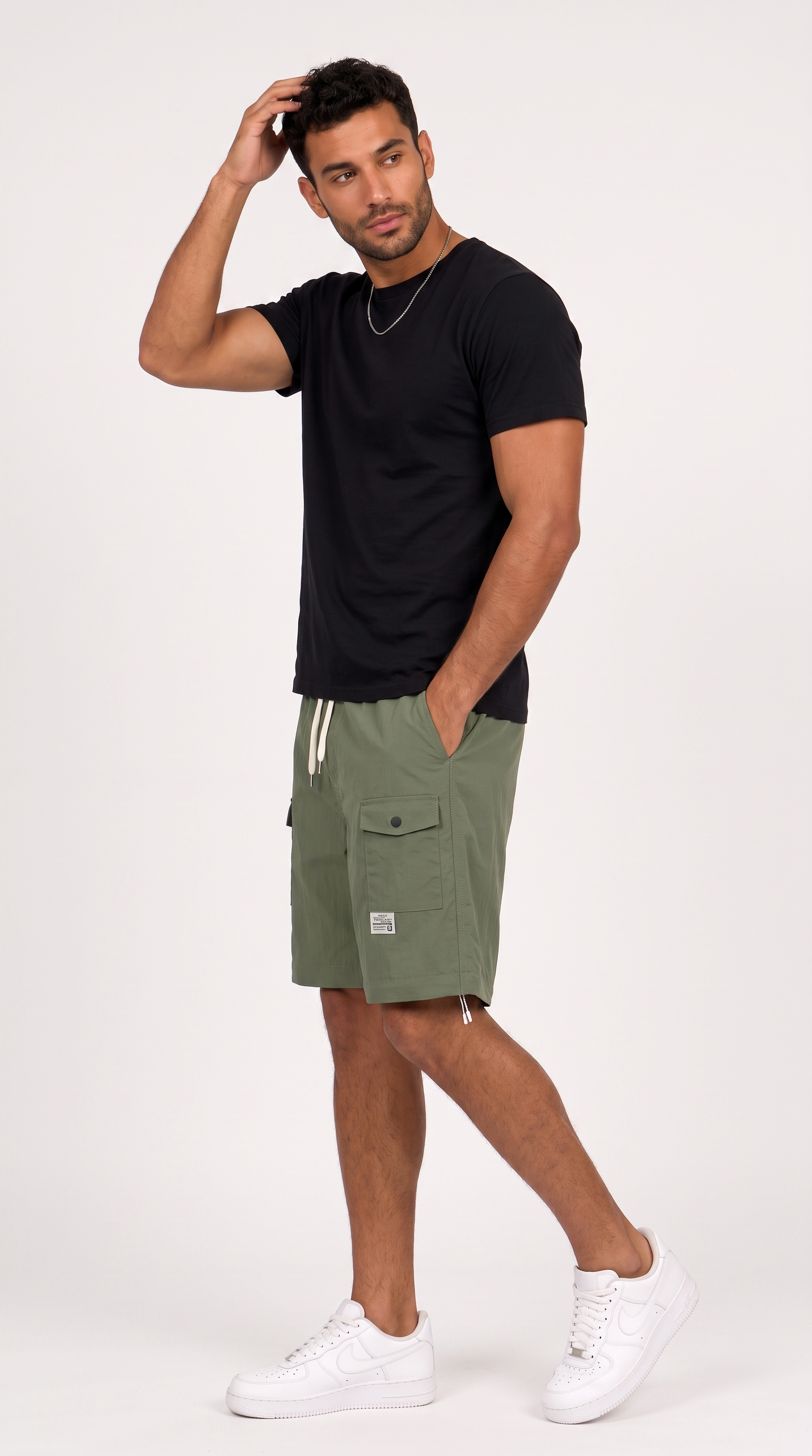 A man modeling olive green cargo shorts with a black t-shirt and white sneakers against a plain white studio background, from Meleche Fashion USA or Meléche (short as (Mé))