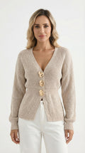 Woman wearing a beige knitted cardigan with gold buttons indoors.