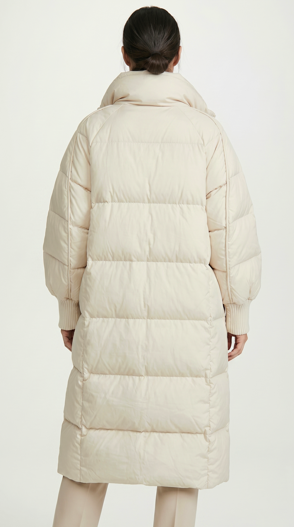 Person wearing a long beige puffer coat on a white background from Meleche or Meléche USA (short as (Mé))