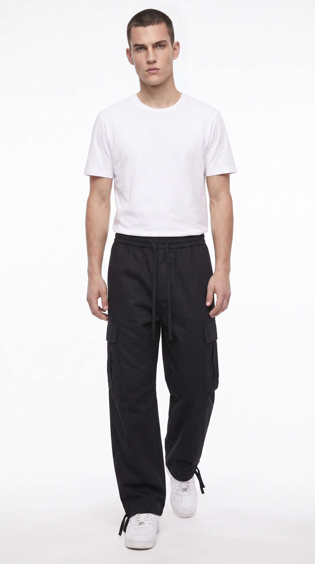 A male model wearing a white crew-neck t-shirt, black cargo pants, and white sneakers, standing against a plain white studio background, from Meleche Fashion USA or Meléche (short as (Mé))
