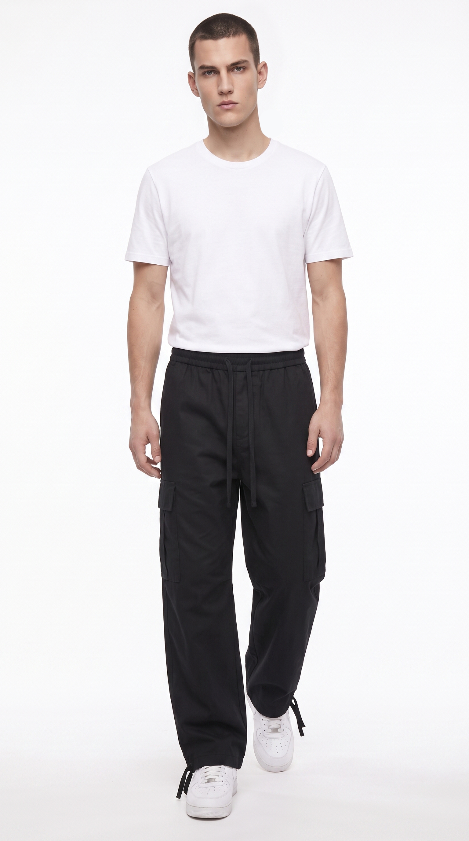 A male model wearing a white crew-neck t-shirt, black cargo pants, and white sneakers, standing against a plain white studio background, from Meleche Fashion USA or Meléche (short as (Mé))