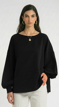 Woman wearing a black poncho and white pants with a plain background
