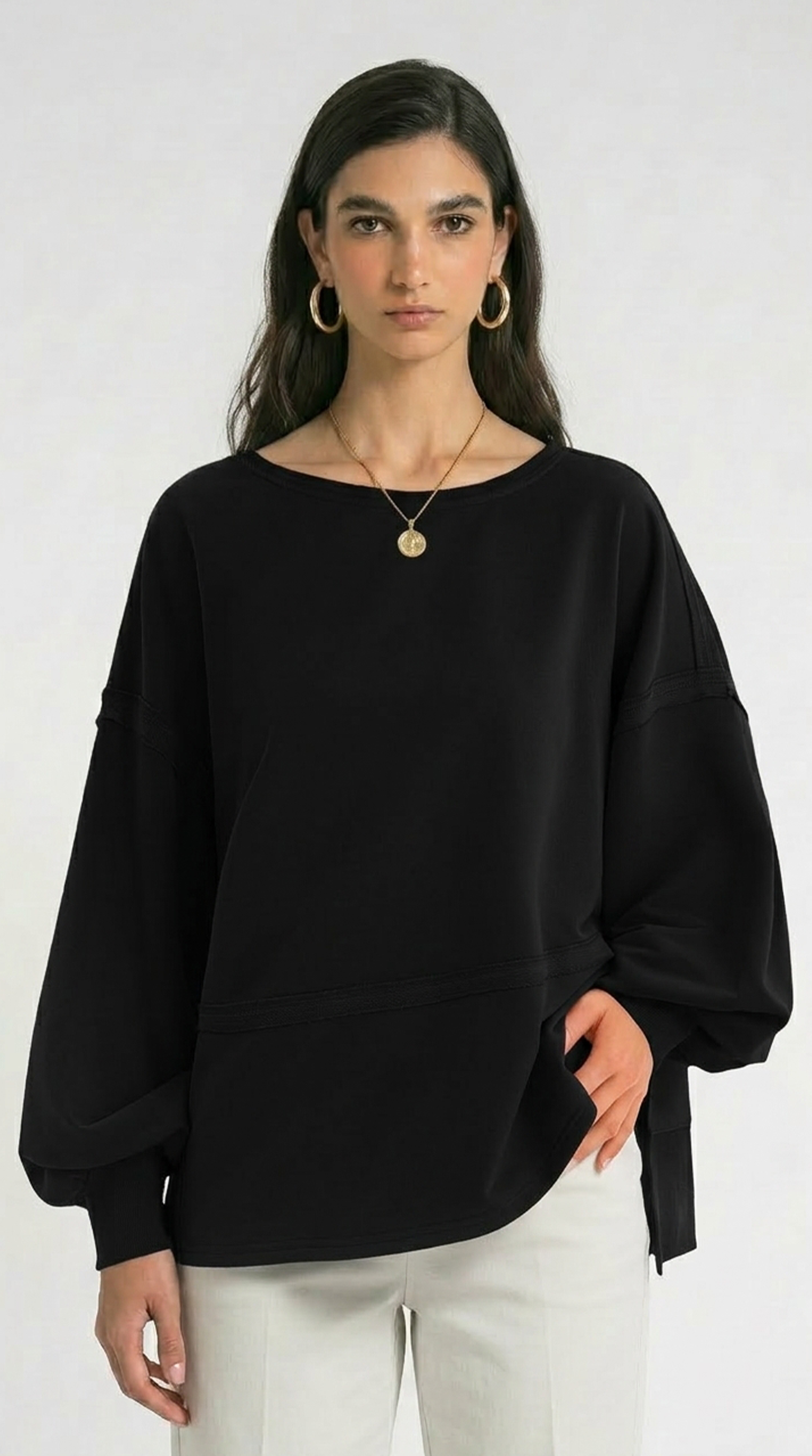 Woman wearing a black poncho and white pants with a plain background