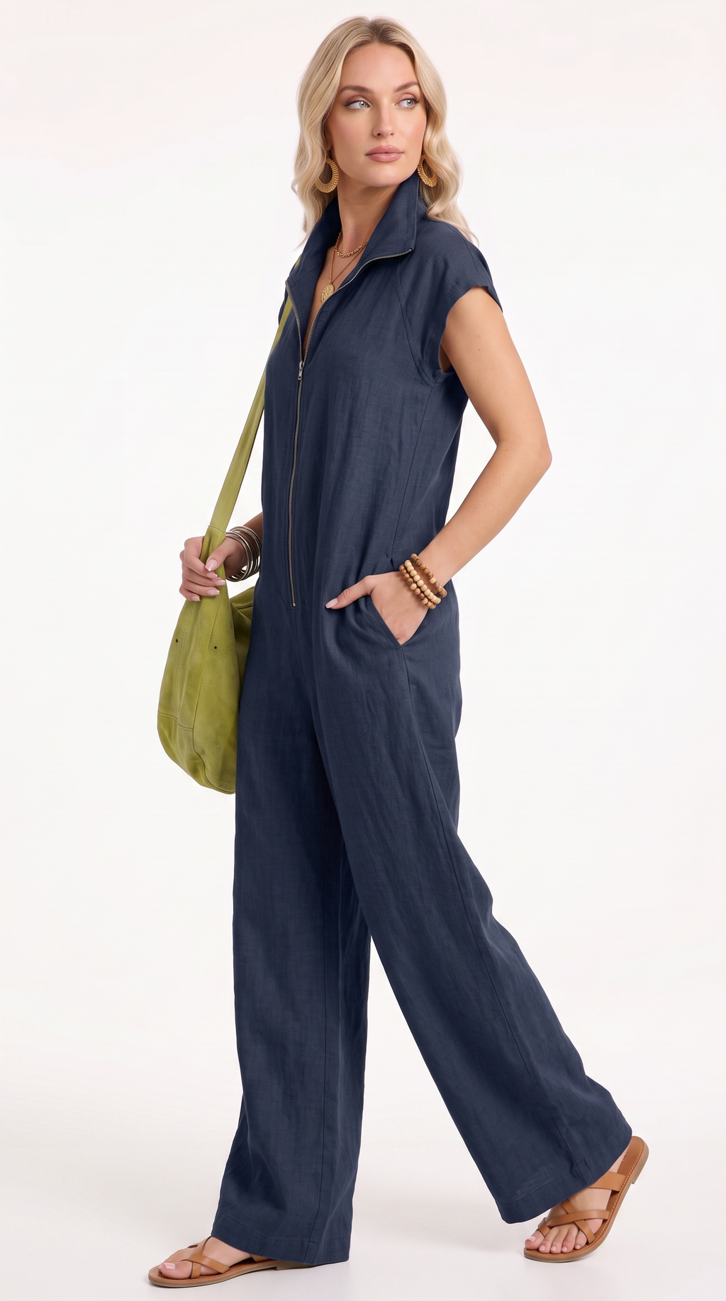 A woman modeling a navy blue sleeveless zip-front jumpsuit with wide legs, holding a green shoulder bag against a plain white studio background, from Meleche Fashion USA or Meléche (short as (Mé))