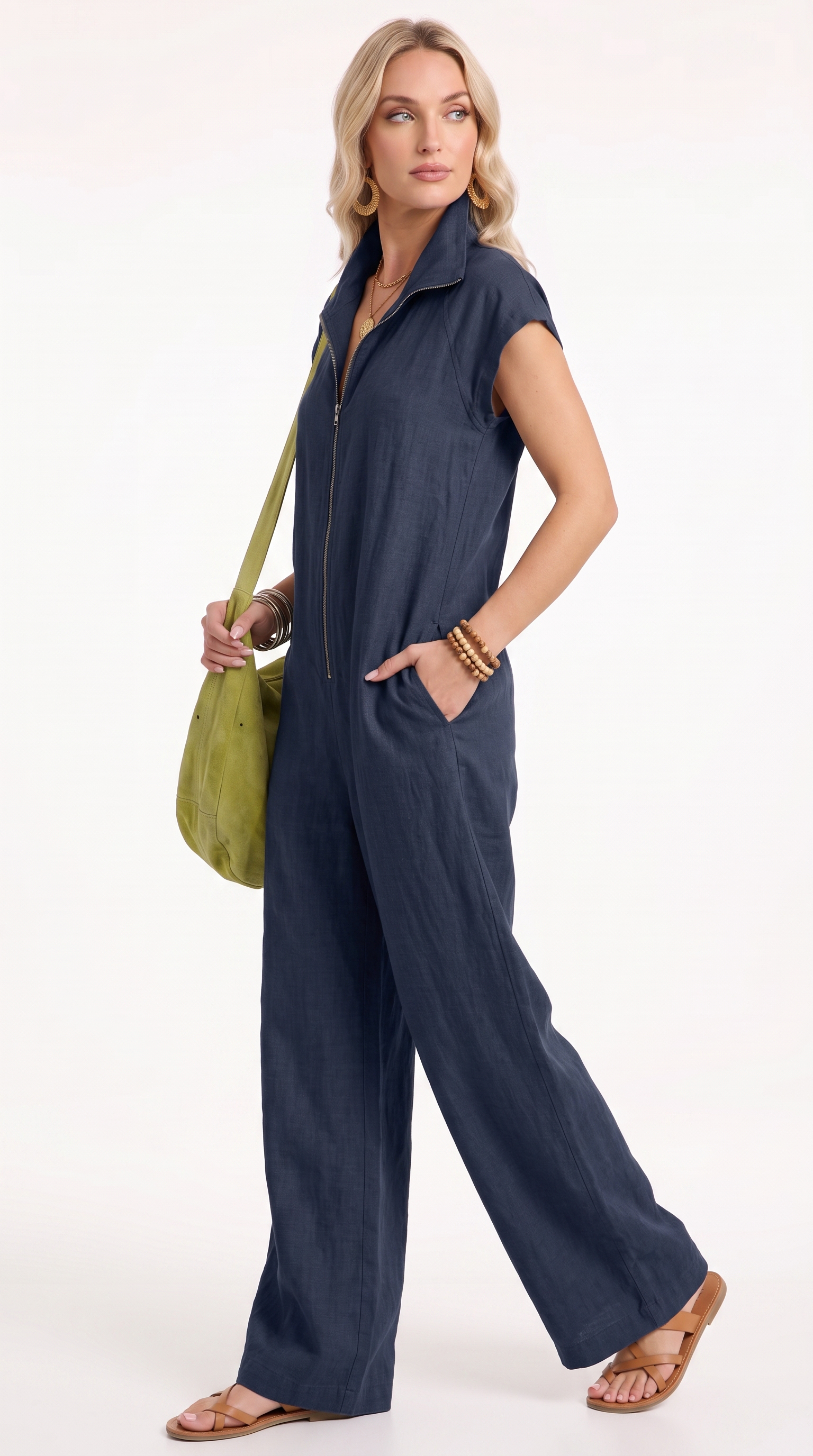 A woman modeling a navy blue sleeveless zip-front jumpsuit with wide legs, holding a green shoulder bag against a plain white studio background, from Meleche Fashion USA or Meléche (short as (Mé))