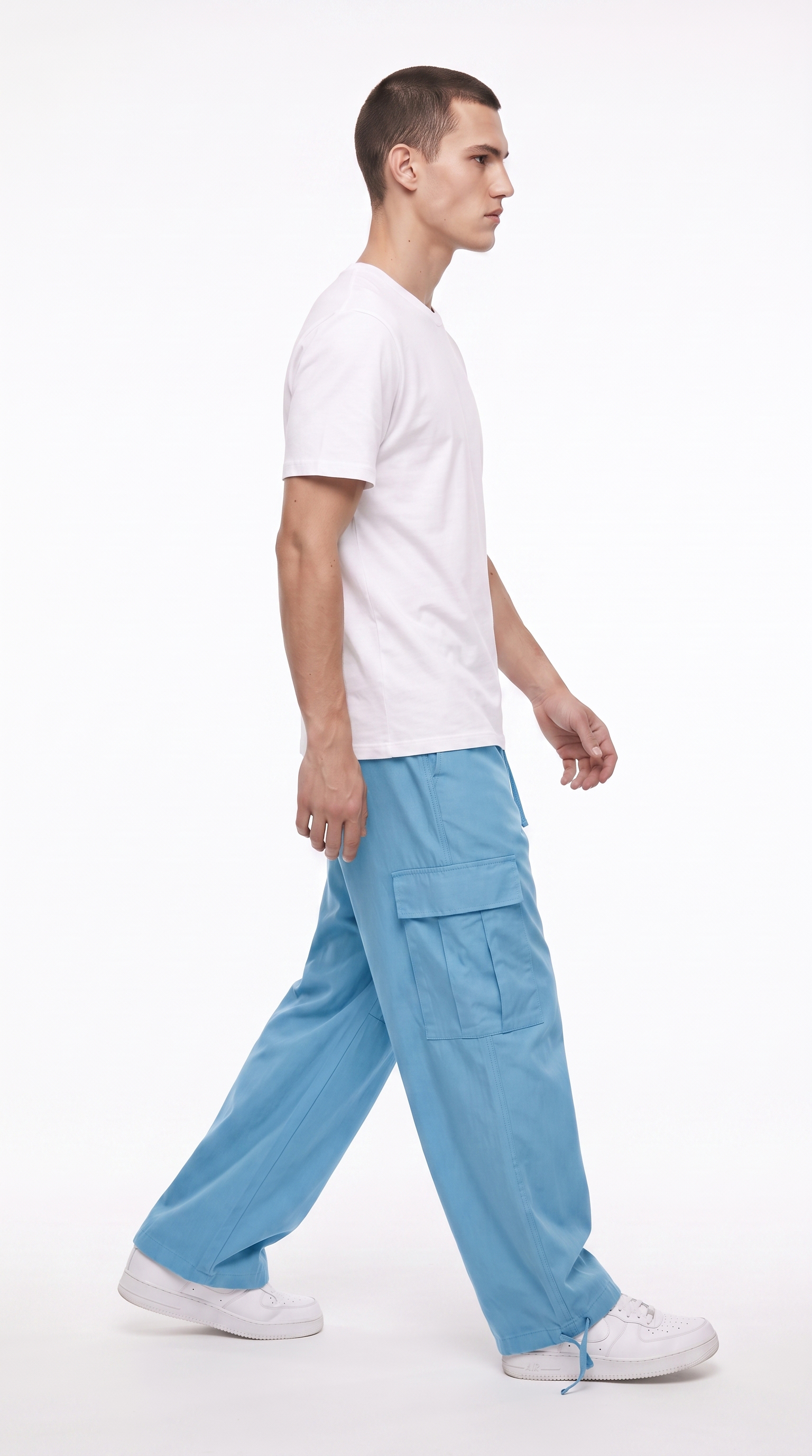 A man in profile wearing a white crew-neck t-shirt, light blue wide-leg cargo pants, and white sneakers, walking against a plain white studio background, from Meleche Fashion USA or Meléche (short as (Mé))