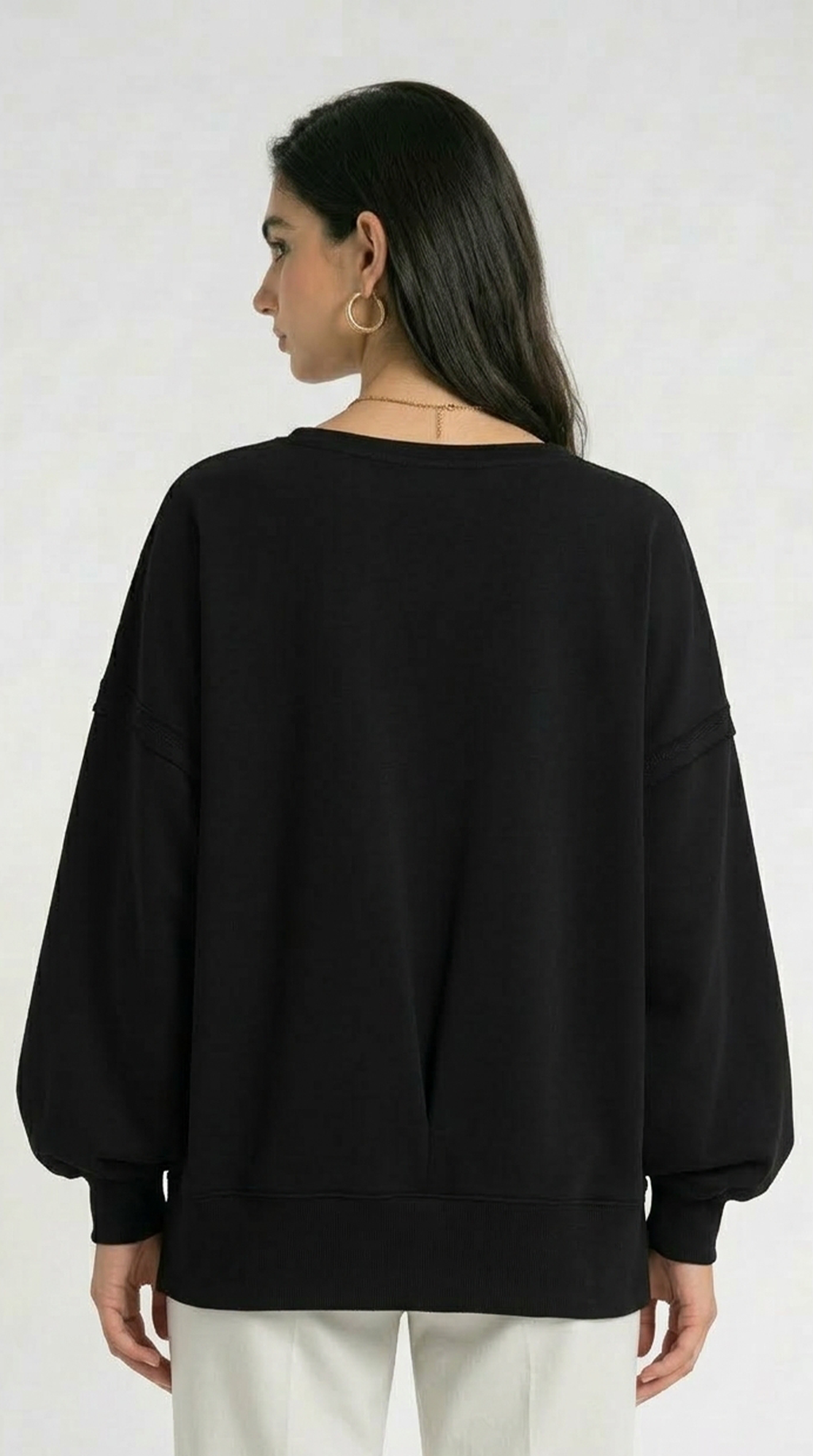 Woman wearing a black poncho over a beige top and white skirt on a white background