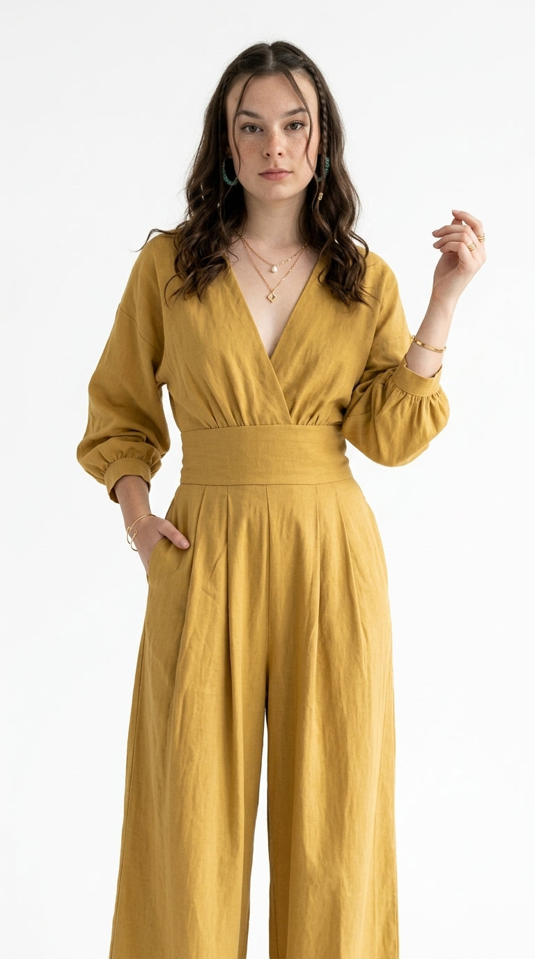 A woman modeling a mustard yellow wide-leg jumpsuit with a wrap-style V-neck bodice, long sleeves, and a matching fabric belt, photographed against a plain white studio background, from Meleche Fashion USA or Meléche (short as (Mé))