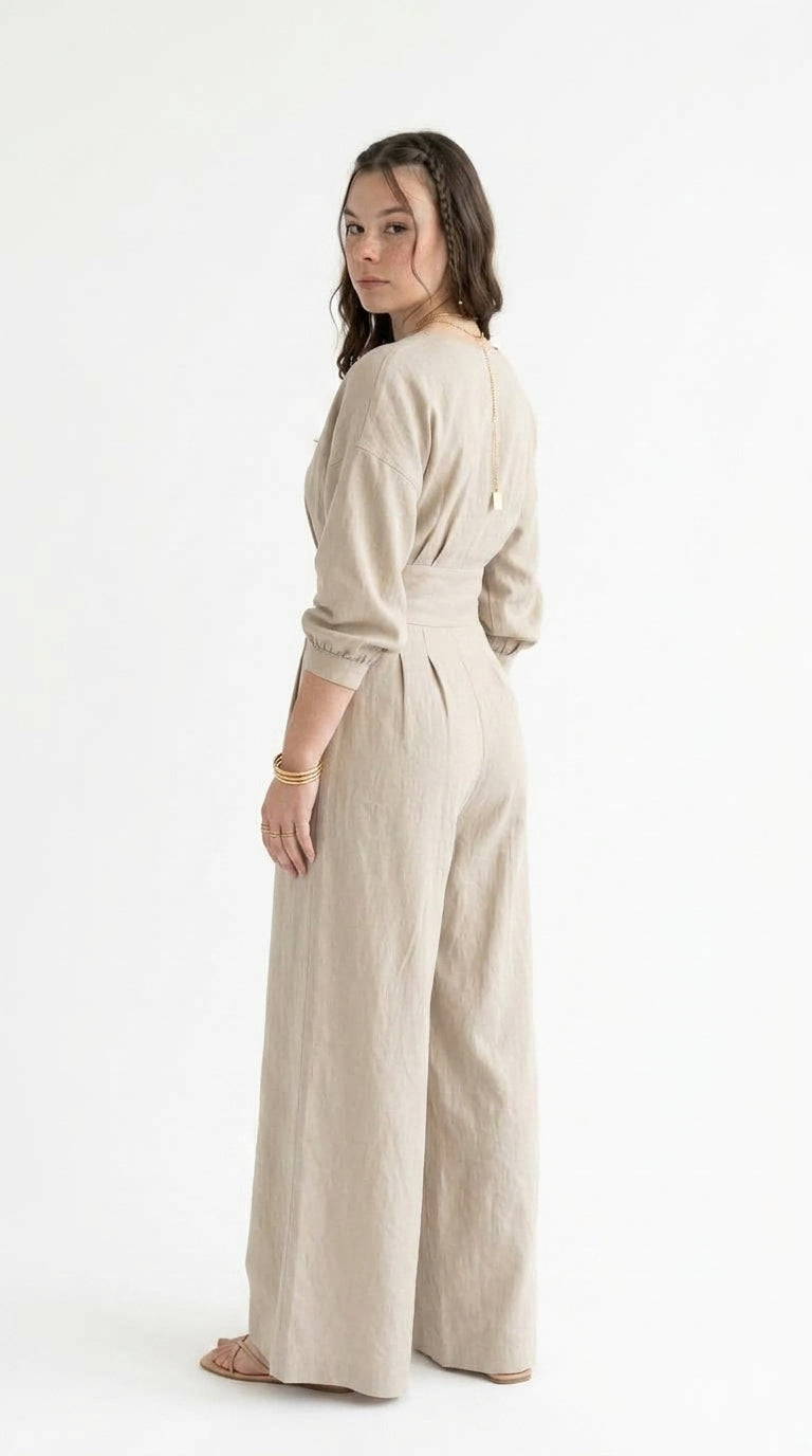 A woman modeling a light beige linen jumpsuit with three-quarter sleeves and wide legs, shown from a side-back angle against a plain white studio background, from Meleche Fashion USA or Meléche (short as (Mé))