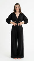 A woman modeling a black long-sleeve wrap-style jumpsuit with wide legs, standing against a plain white studio background, from Meleche Fashion USA or Meléche (short as (Mé))