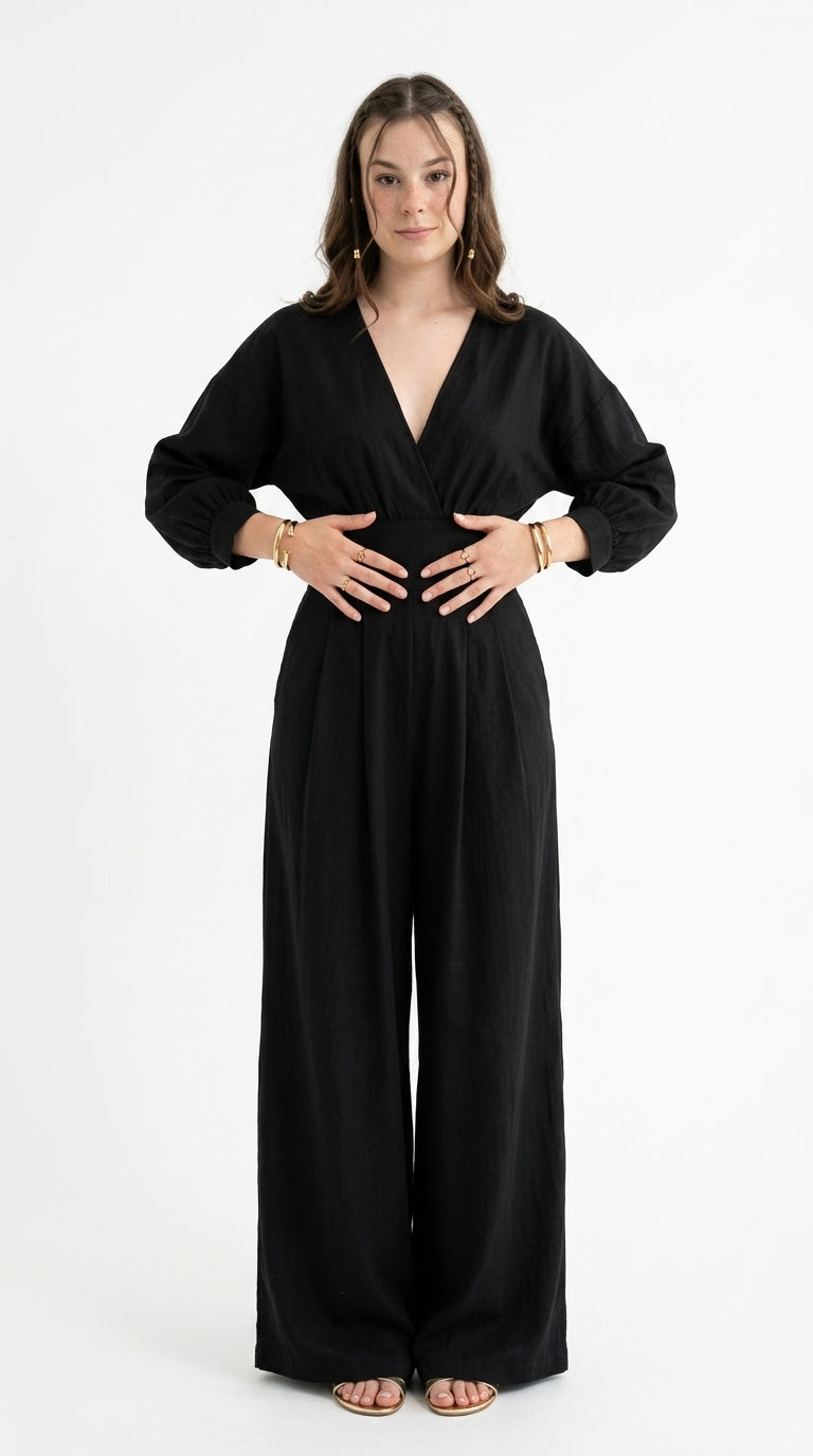 A woman modeling a black long-sleeve wrap-style jumpsuit with wide legs, standing against a plain white studio background, from Meleche Fashion USA or Meléche (short as (Mé))