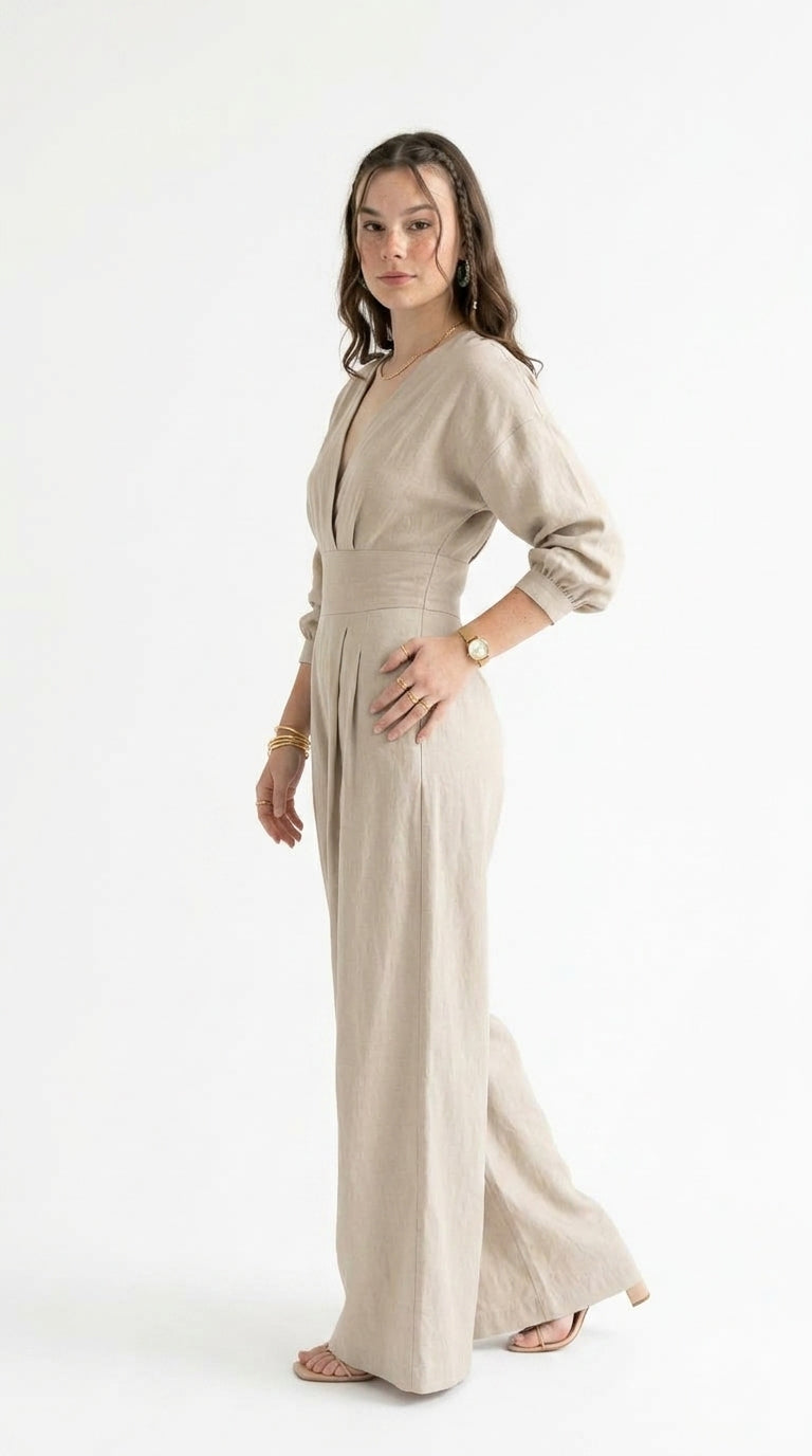 A woman modeling a light beige linen jumpsuit with three-quarter sleeves and a deep V-neckline, standing against a plain white studio background, from Meleche Fashion USA or Meléche (short as (Mé))