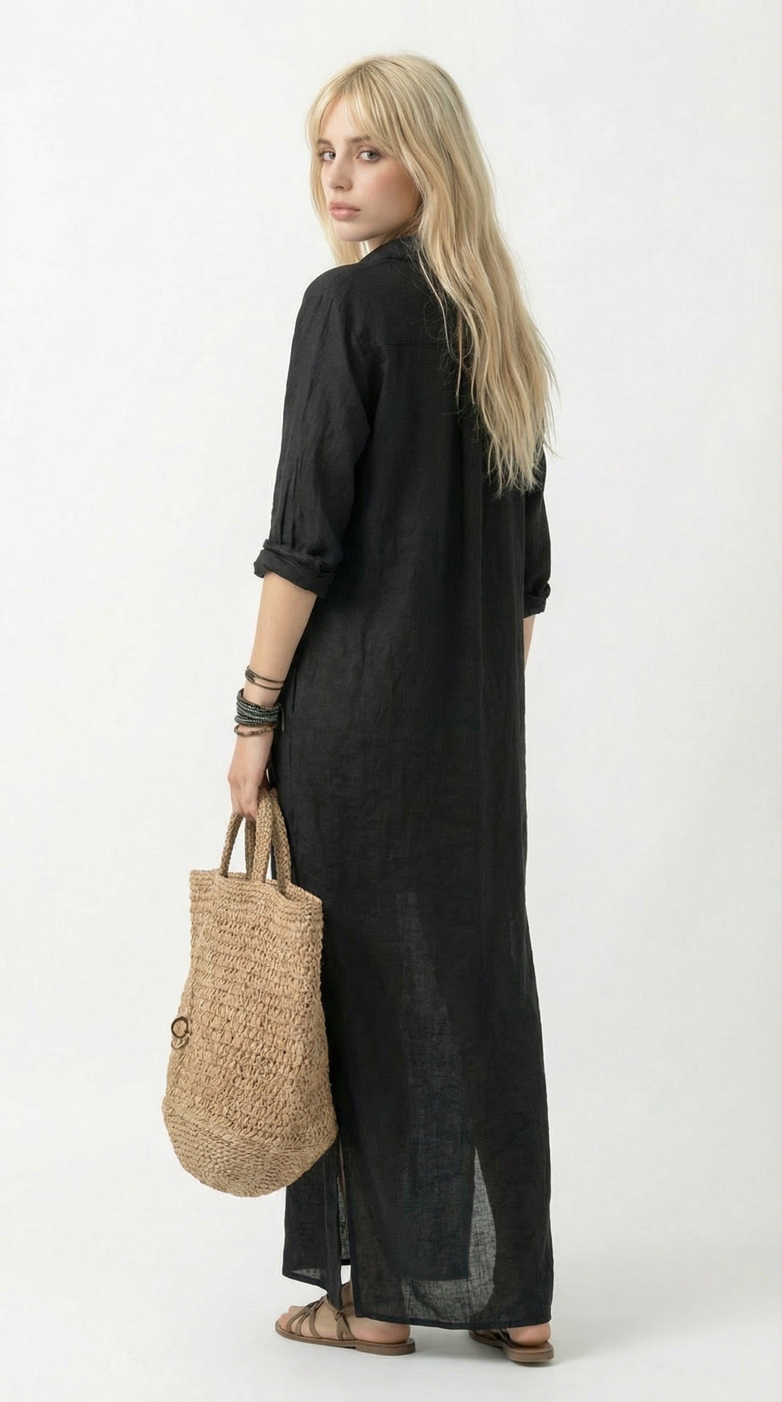 Person wearing a black dress holding a woven bag against a gray wall.