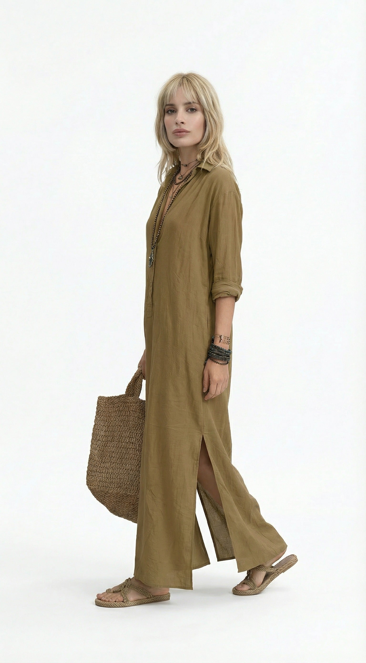 Woman wearing a long olive green dress holding a woven bag against a gray background