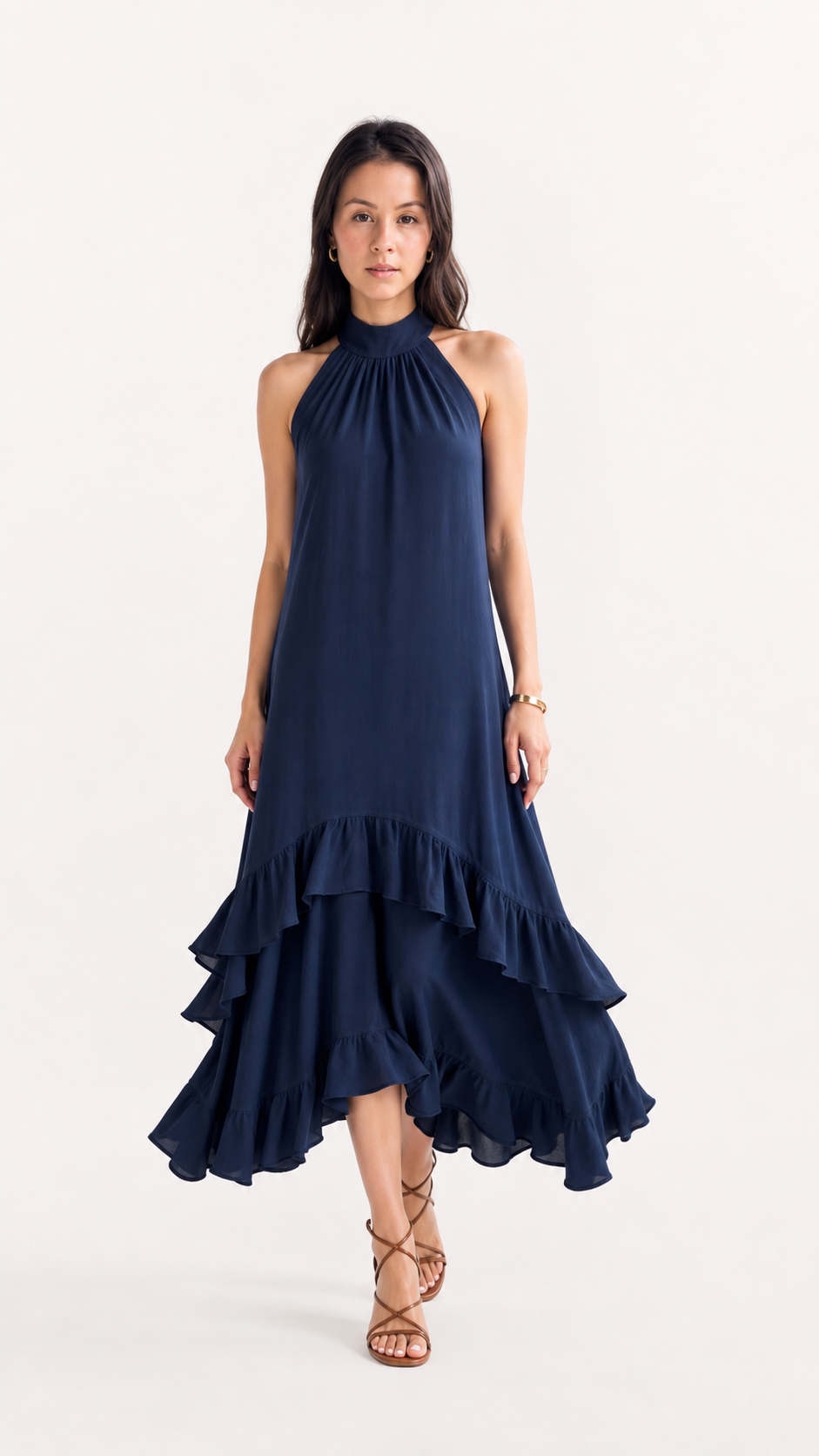 A woman modeling a sleeveless navy blue halter-neck midi dress with a tiered ruffled skirt, paired with brown strappy high-heeled sandals, against a plain white studio background, from Meleche Fashion USA or Meléche (short as (Mé))