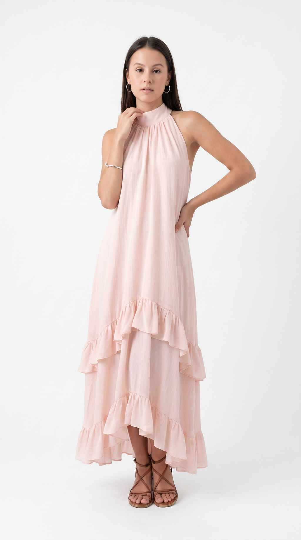 A woman modeling a light pink halter-neck maxi dress with a tiered ruffle hem, paired with brown strappy sandals, against a plain white studio background, from Meleche Fashion USA or Meléche (short as (Mé))