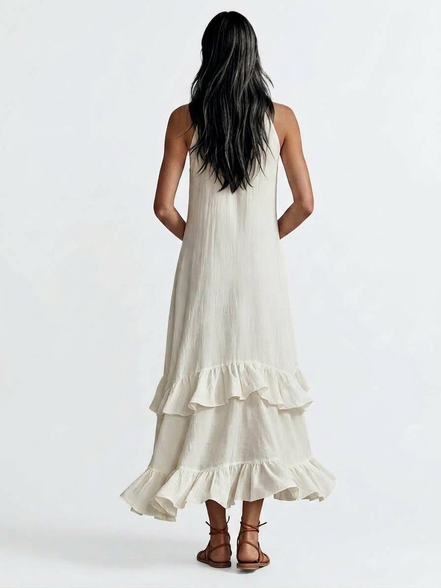A woman viewed from behind wearing a sleeveless, tiered maxi dress in a warm off-white or cream color, paired with brown strappy sandals, against a plain white studio background, from Meleche Fashion USA or Meléche (short as (Mé))