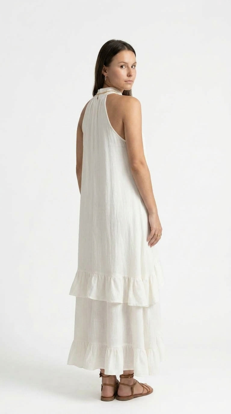 A woman modeling a sleeveless, high-neck, tiered maxi dress in off-white, shown from a three-quarters back view against a plain white studio background, from Meleche Fashion USA or Meléche (short as (Mé))