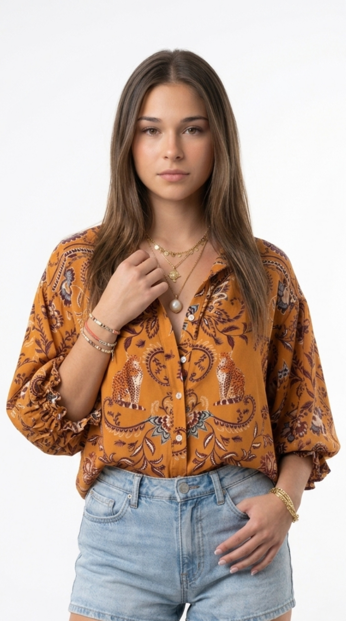 A woman modeling a mustard yellow button-up blouse with a brown and black paisley pattern, paired with light blue denim shorts, against a plain white background, from Meleche Fashion or Meléche (short as (Mé)) and shoot taken by Meléche studio photography NYC-USA