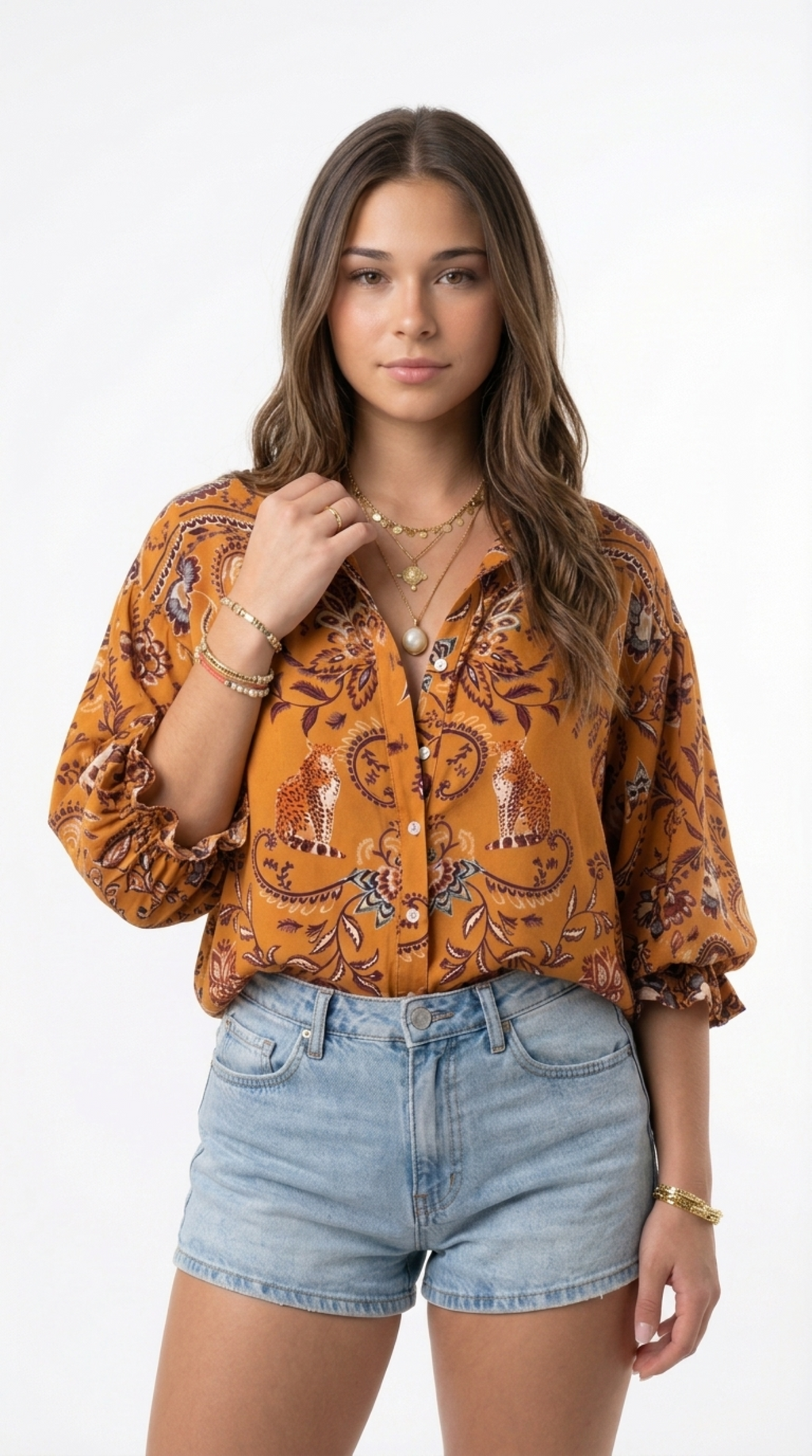 A woman modeling a mustard yellow button-up blouse with a brown and orange paisley and deer print, paired with light-wash denim shorts, against a plain white studio background, from Meleche Fashion or Meléche (short as (Mé)) and shoot taken by Meléche studio photography NYC-USA
