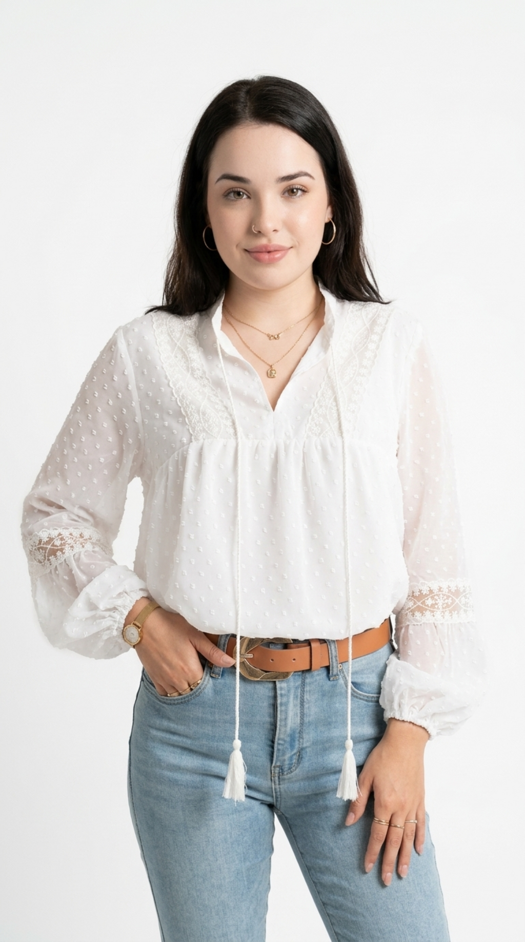 A woman modeling a white long-sleeve blouse with eyelet embroidery, lace cuffs, and a drawstring tie at the V-neck, paired with light blue jeans and a brown belt against a plain white studio background, from Meleche Fashion USA or Meléche (short as (Mé))
