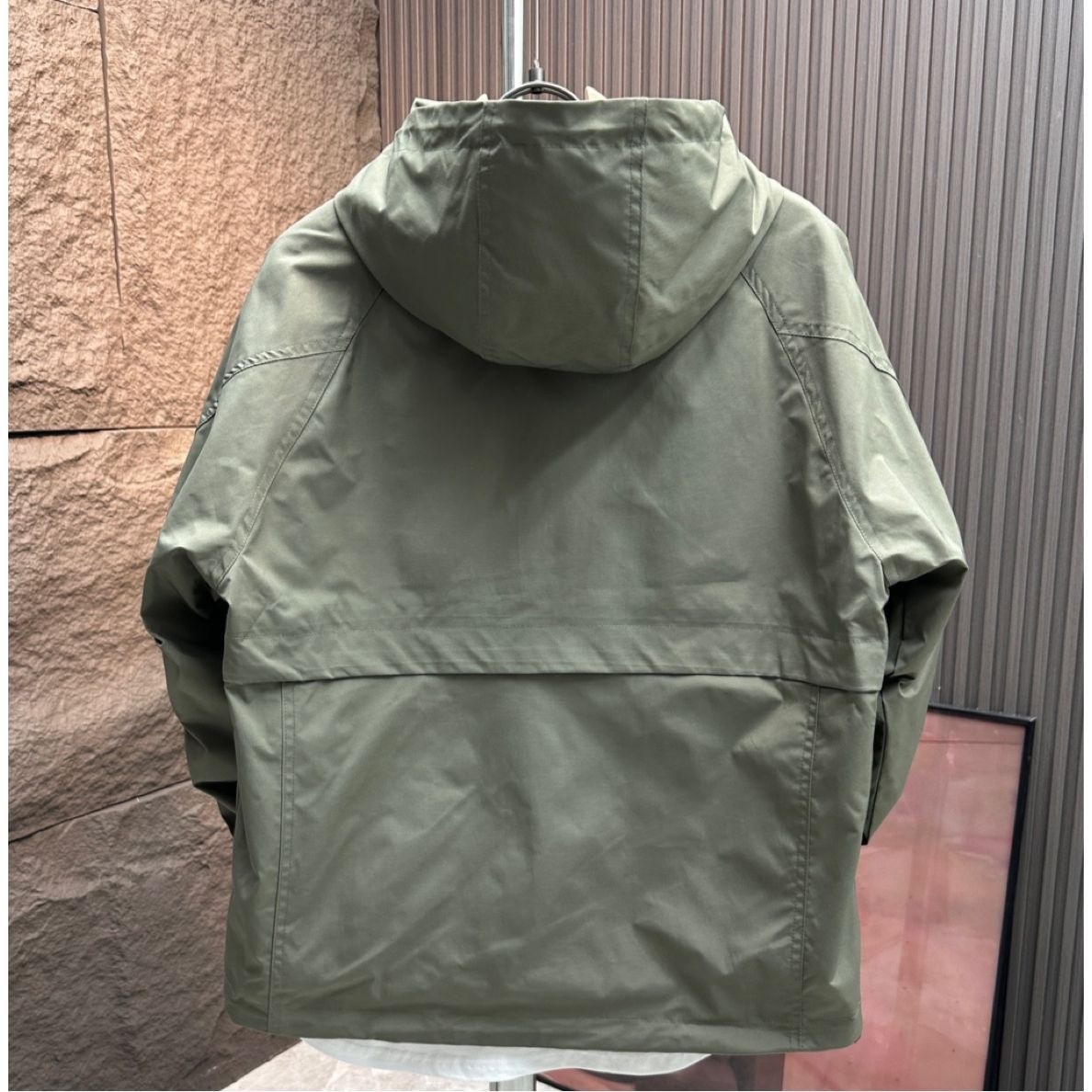 Green hooded jacket on a hanger against a textured wall.