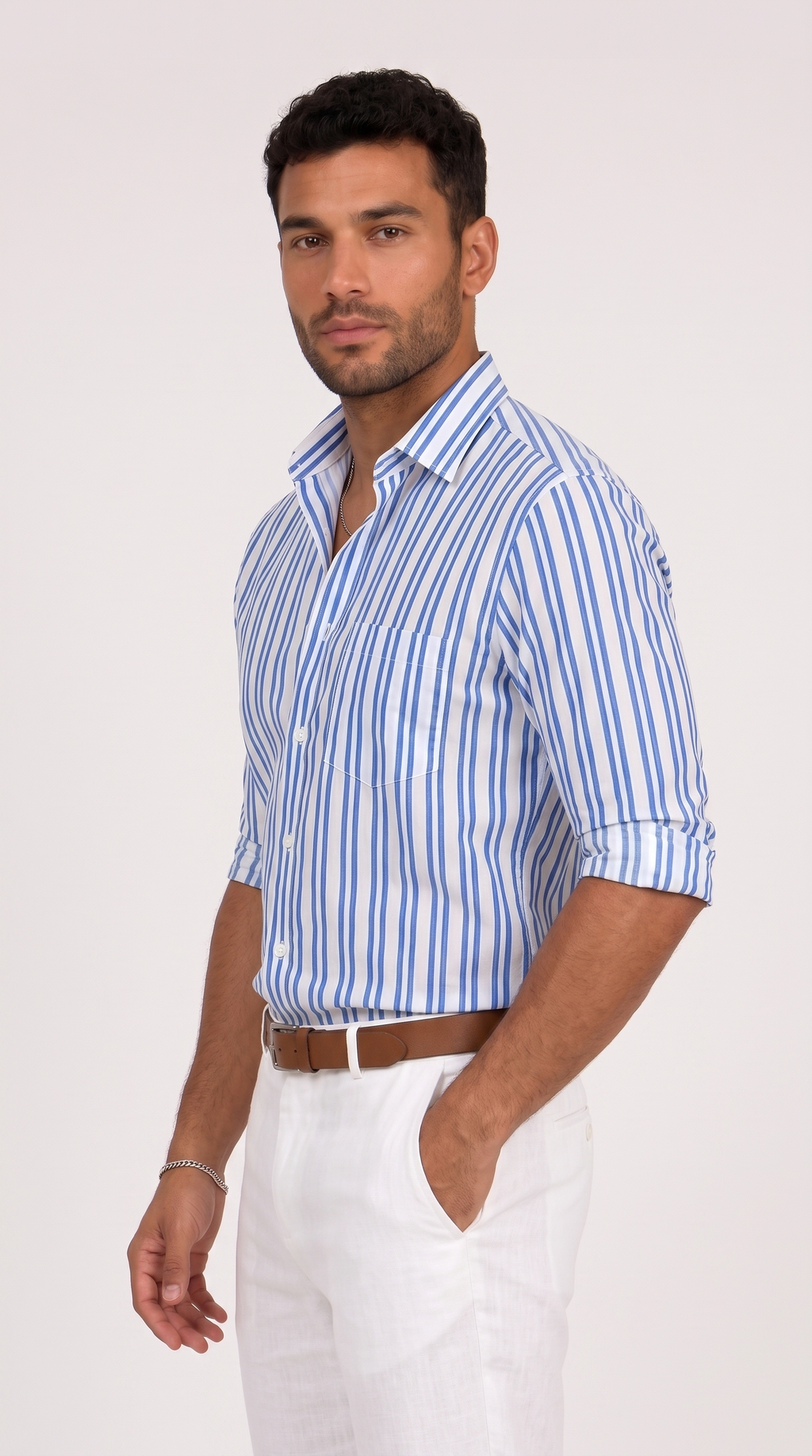 A man wearing a blue and white vertically striped button-down shirt with white trousers and a brown belt, standing against a plain light background, from Meleche Fashion USA or Meléche (short as (Mé))