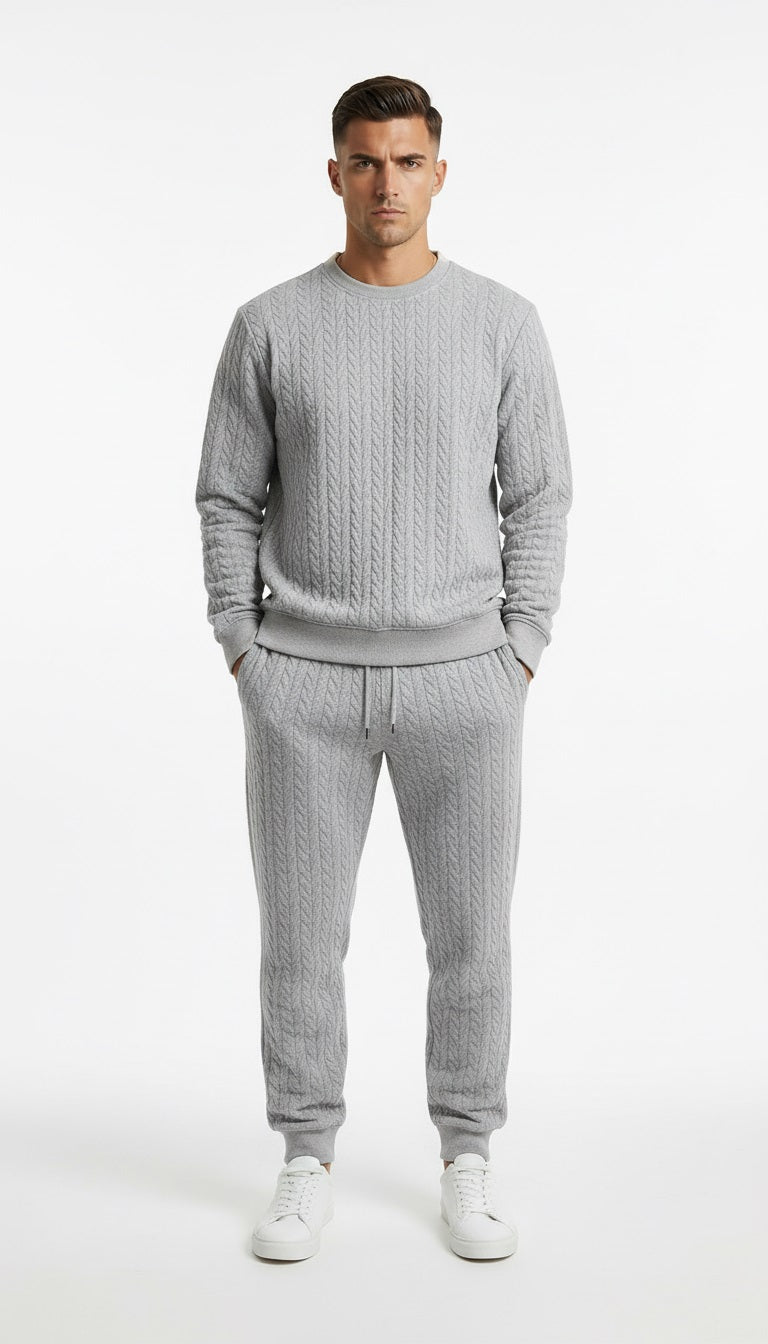 Man wearing a gray cable knit sweater and matching pants on a white background