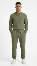 Man in olive green outfit standing on a balcony with ocean view and yachts.
