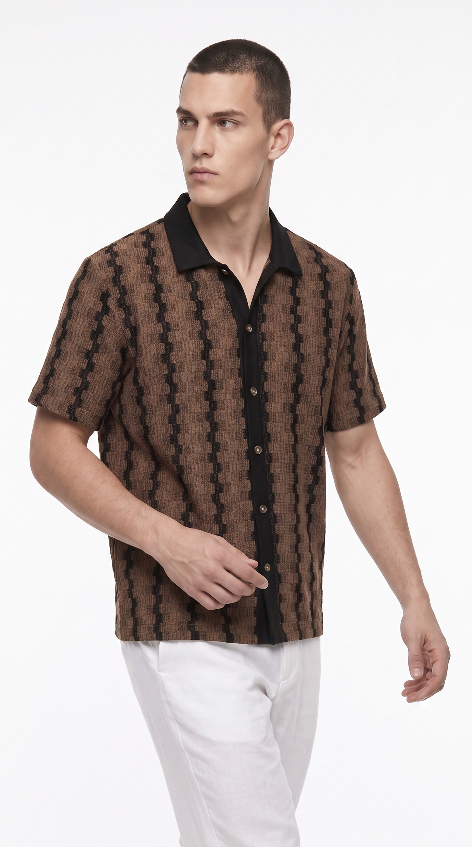A man wearing a brown and black patterned short-sleeve button-up shirt with a black collar, paired with white pants, photographed against a clean white studio background, from Meleche Fashion USA or Meléche (short as (Mé))