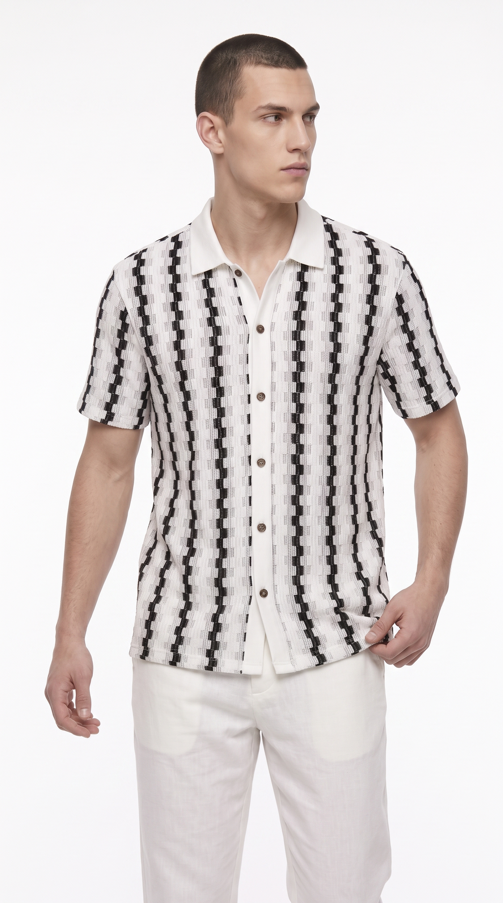 A man wearing a short-sleeve button-up shirt with a black and white geometric pattern, paired with white trousers, photographed against a plain white studio background, from Meleche Fashion USA or Meléche (short as (Mé))