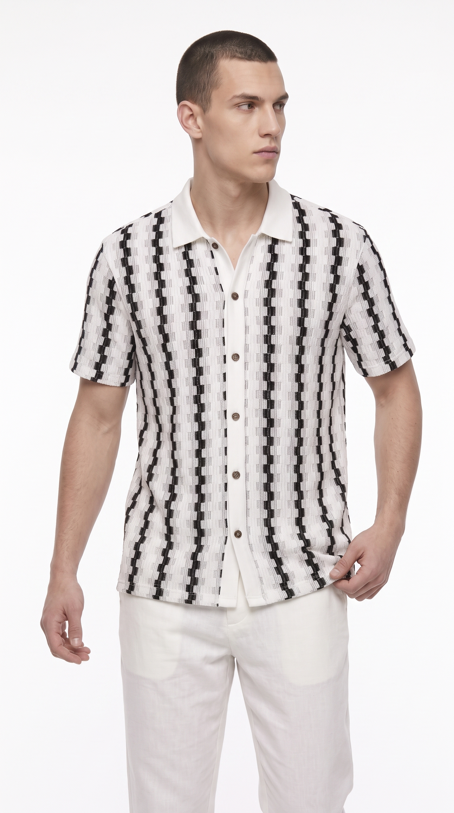 A man wearing a short-sleeve button-up shirt with a black and white geometric pattern, paired with white trousers, photographed against a plain white studio background, from Meleche Fashion USA or Meléche (short as (Mé))