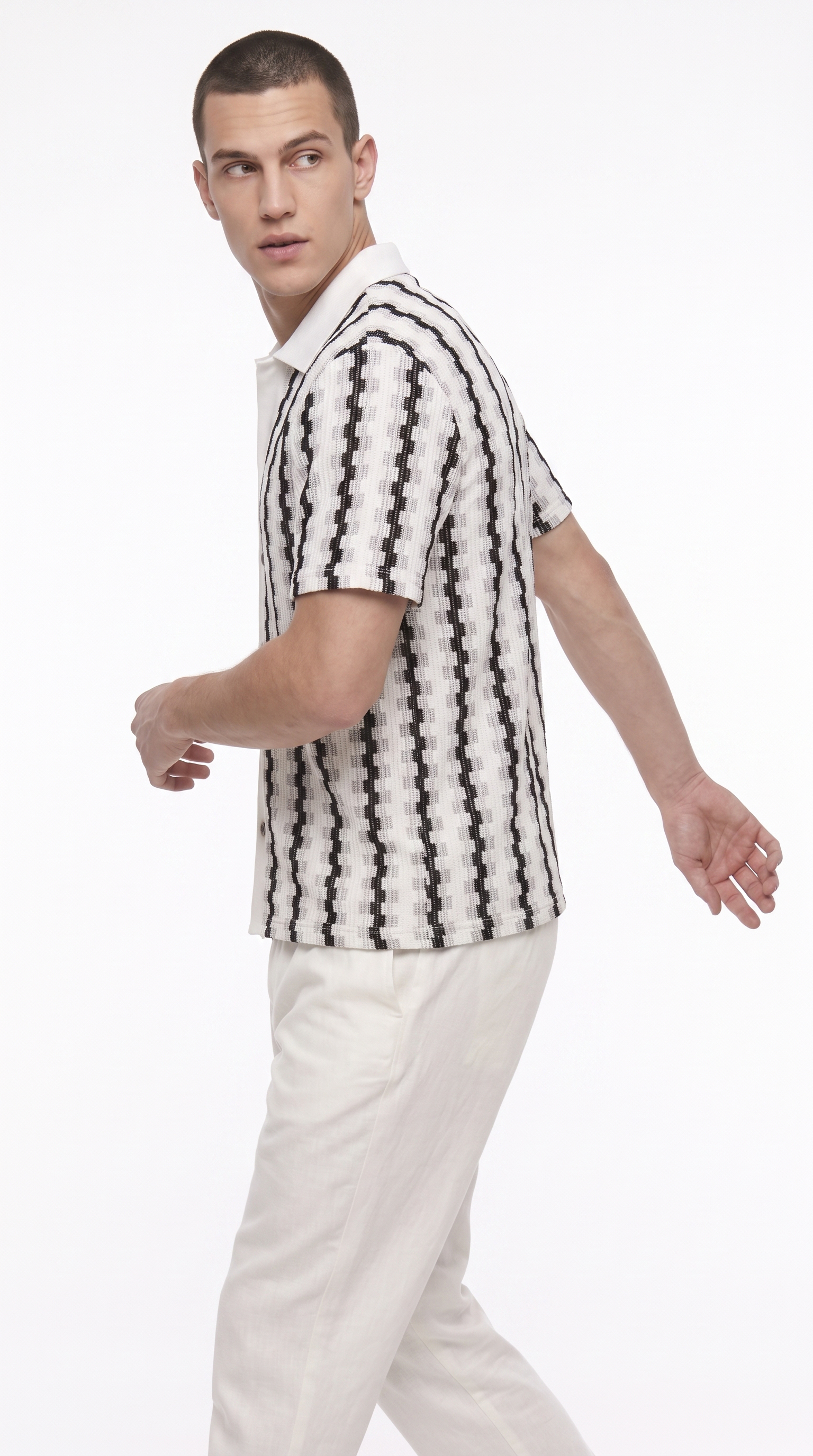 A man wearing a short-sleeve collared shirt with a black and white geometric pattern, paired with off-white trousers, photographed against a plain white studio background, from Meleche Fashion USA or Meléche (short as (Mé))
