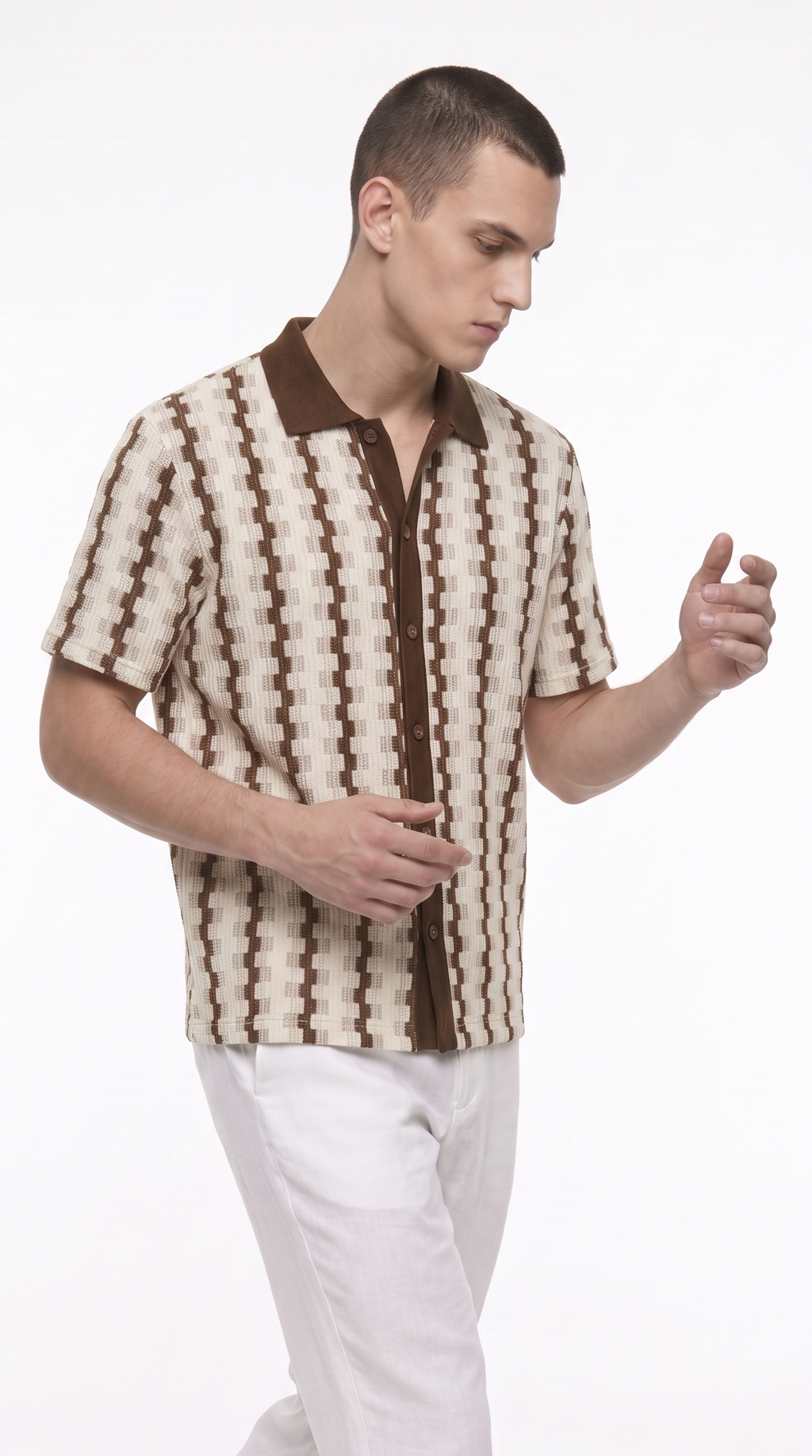 A man wearing a brown and cream geometric patterned short-sleeve button-up shirt with white trousers, standing against a plain white studio background, from Meleche Fashion USA or Meléche (short as (Mé))