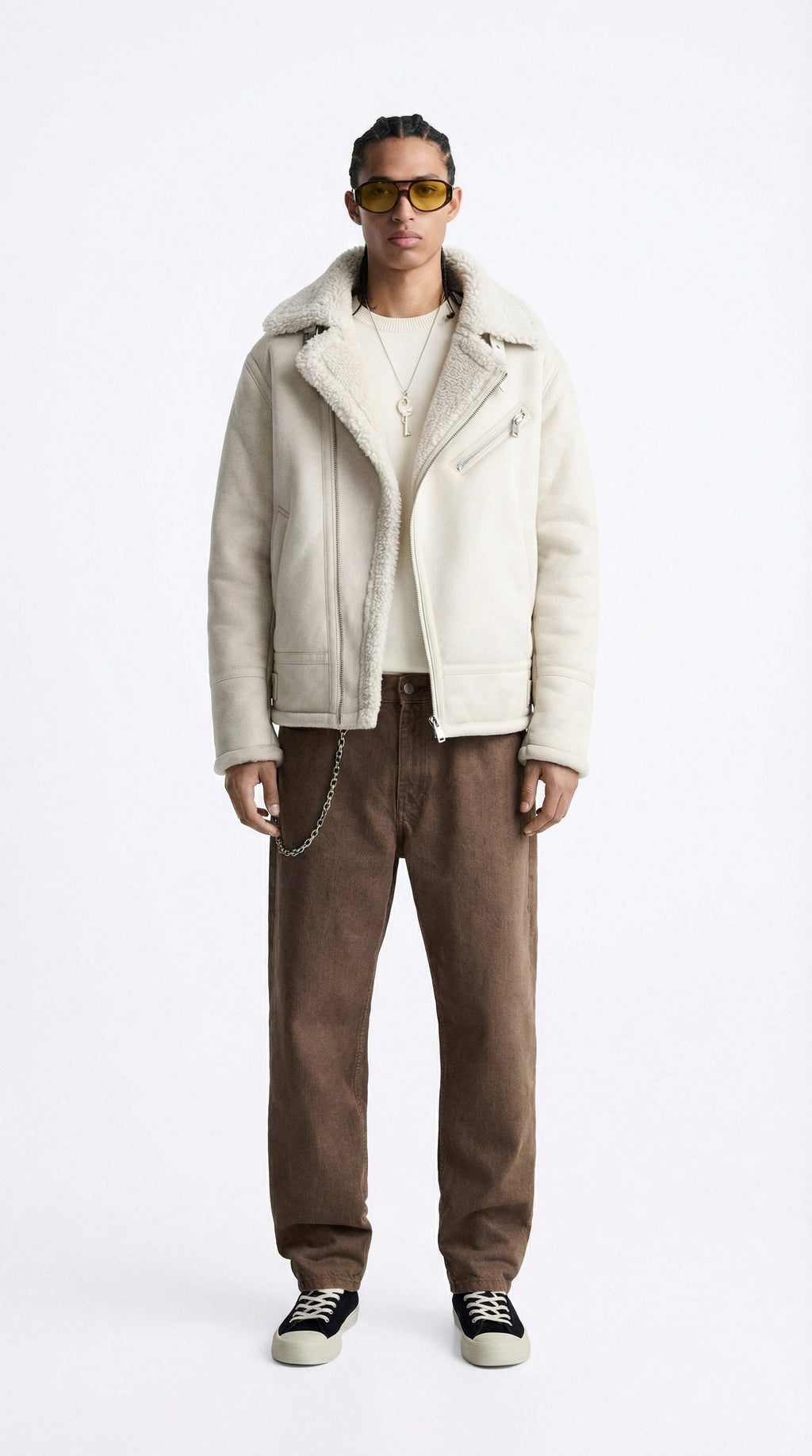 Person wearing a beige jacket and brown pants on a white background