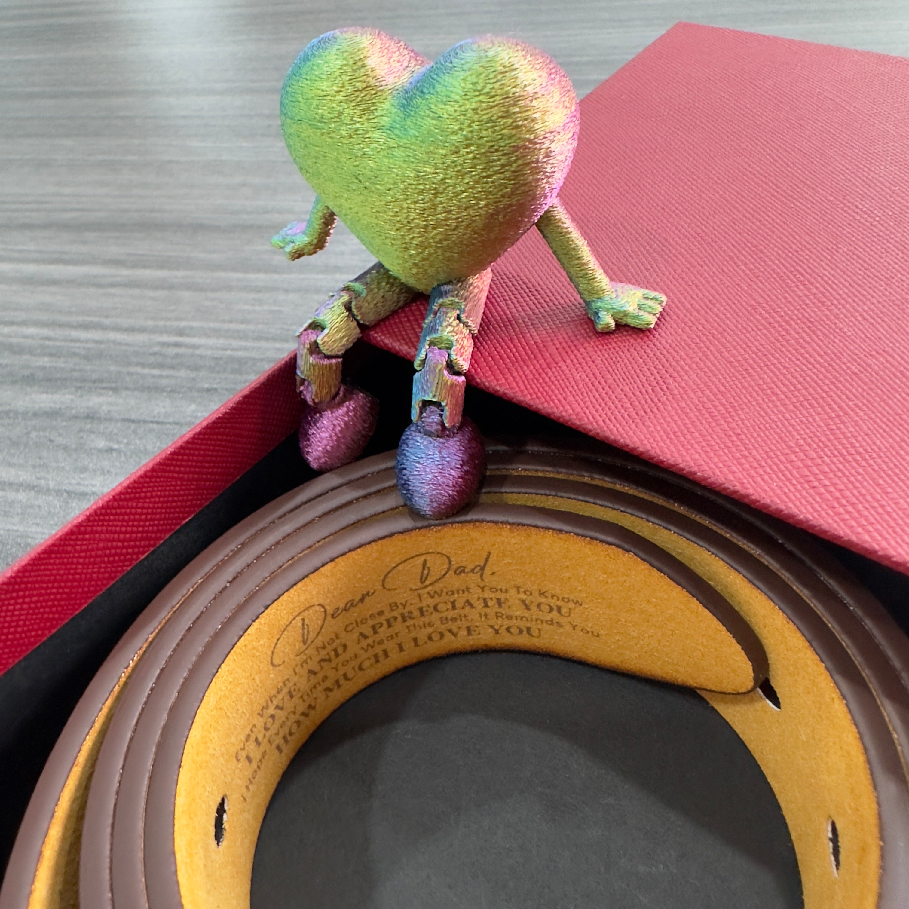 Gael belt Colorful heart-shaped plush toy on a red book with a wooden frame underneath from Meleche or Meléche (short as (Mé))