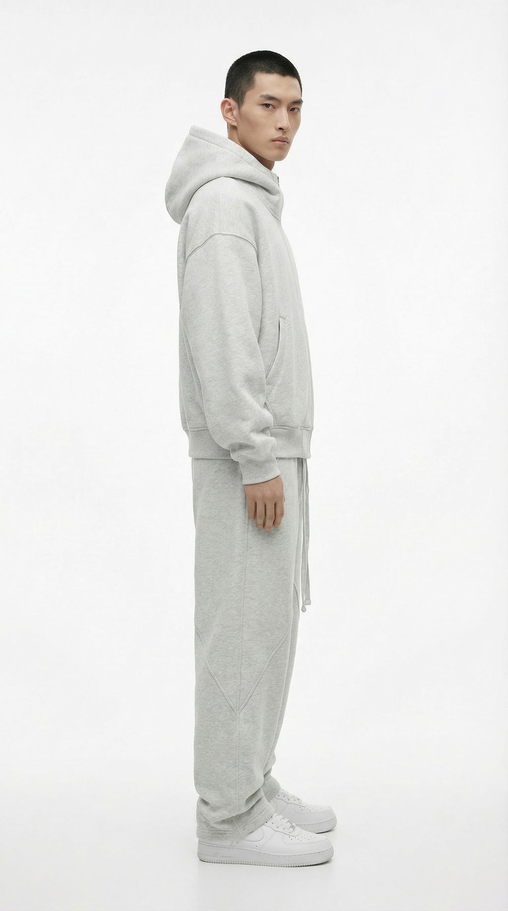 Person wearing a gray tracksuit and white sneakers against a concrete wall.