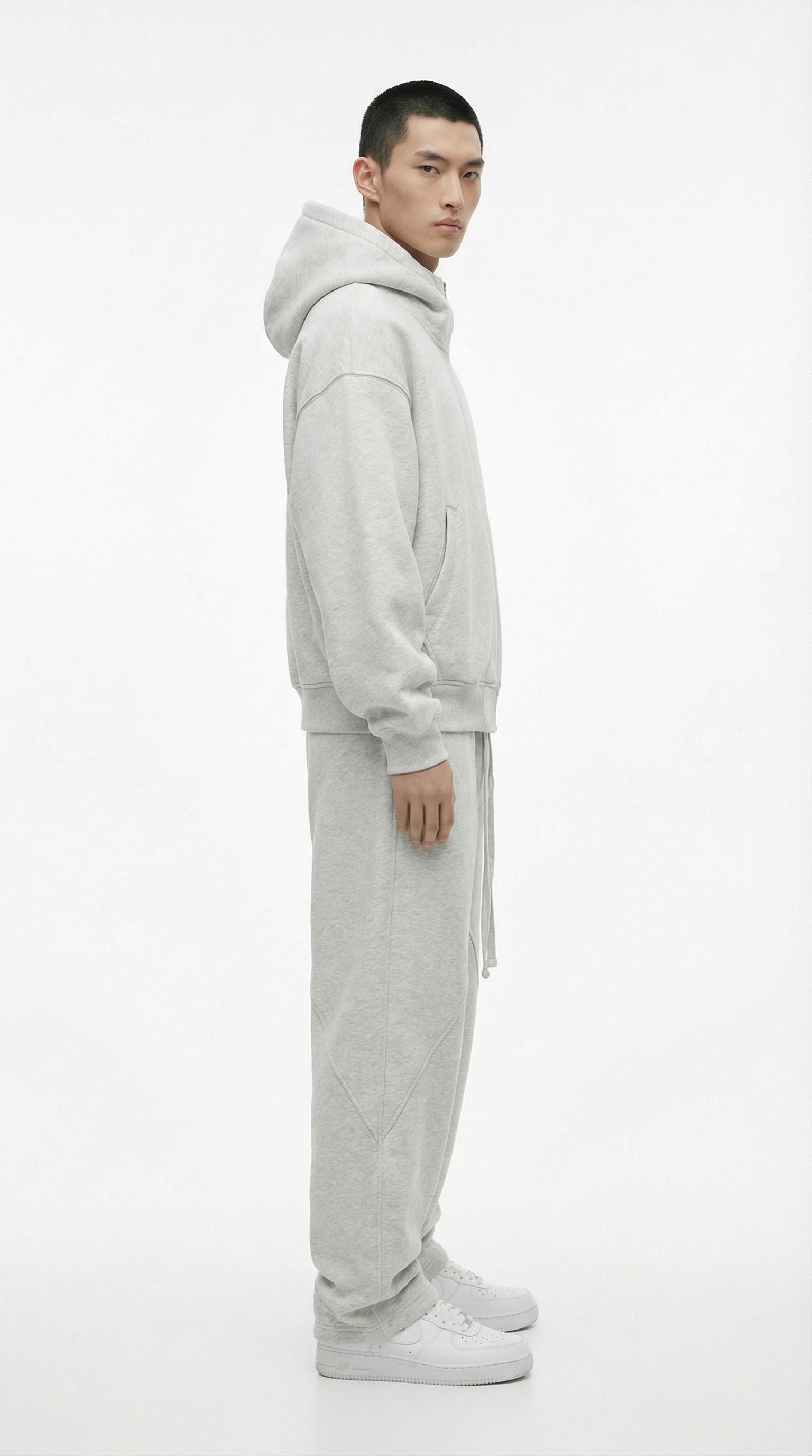 Person wearing a gray tracksuit and white sneakers against a concrete wall.