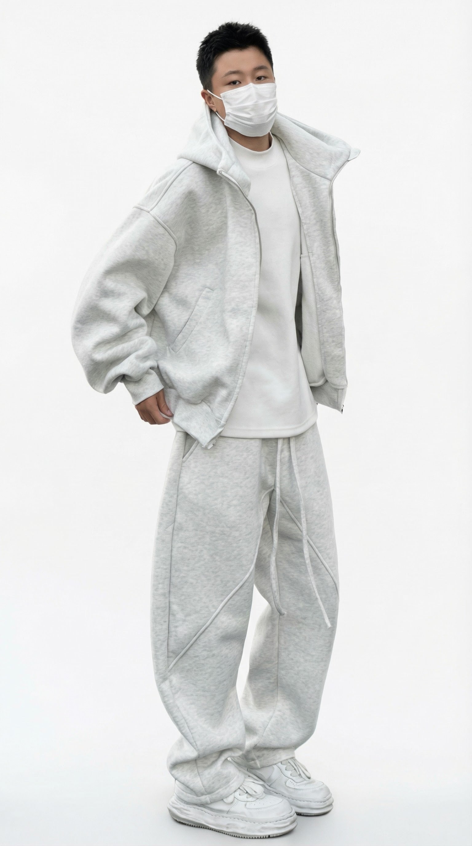 Person wearing a light gray tracksuit and white sneakers against a concrete wall.