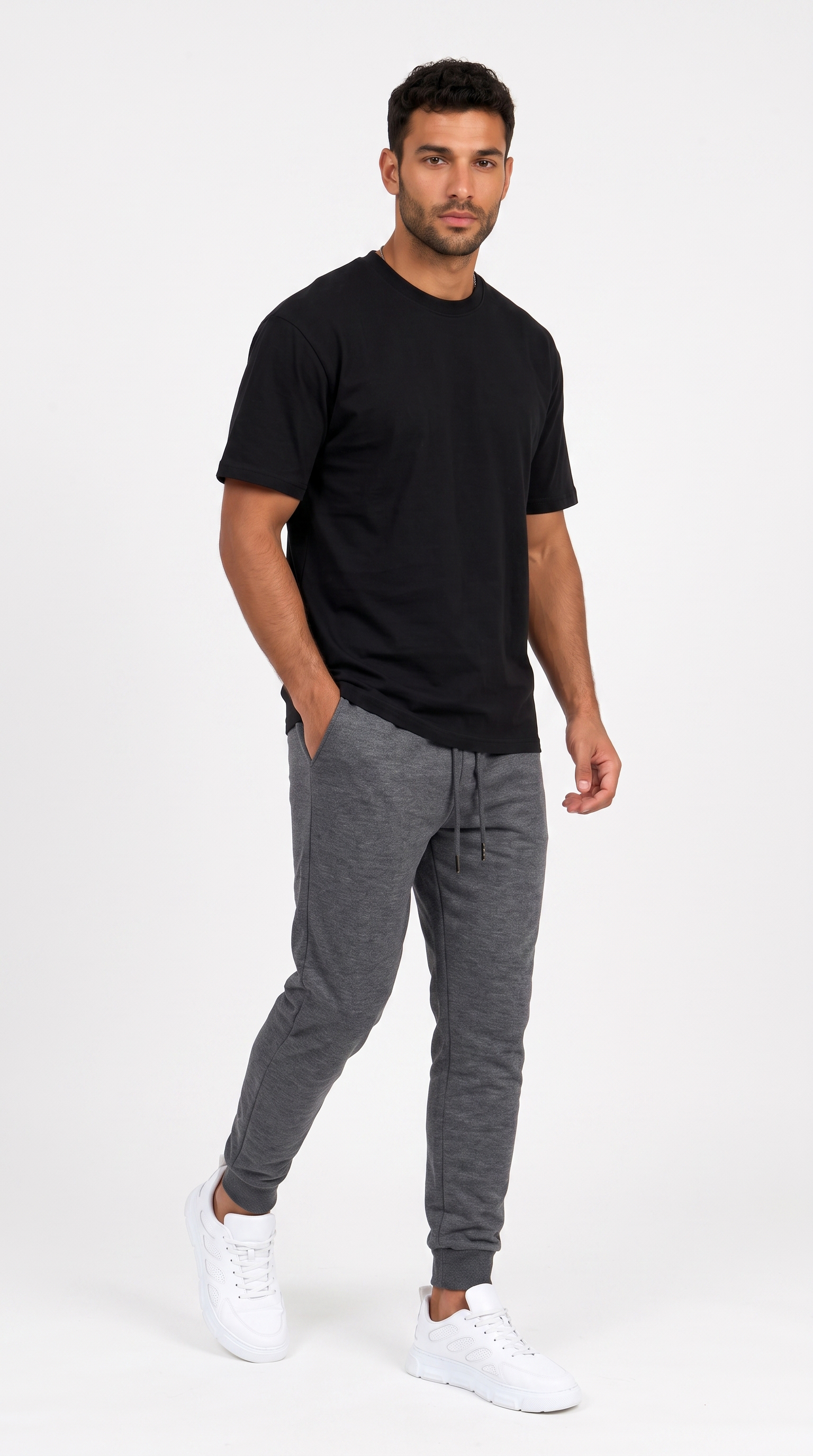 A man modeling a black crewneck t-shirt and heather gray jogger pants with white sneakers, standing against a plain light gray studio background, from Meleche Fashion USA or Meléche (short as (Mé))
