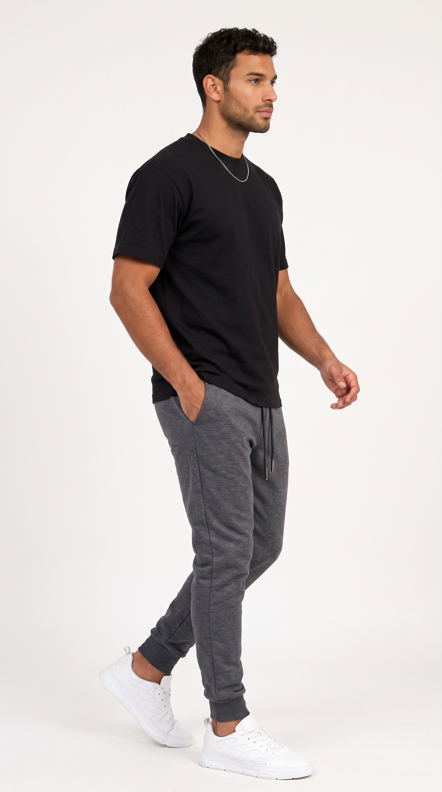 A man wearing a black crew-neck t-shirt, dark gray heather jogger sweatpants, and white sneakers, shown in profile against a plain white studio background, from Meleche Fashion USA or Meléche (short as (Mé))