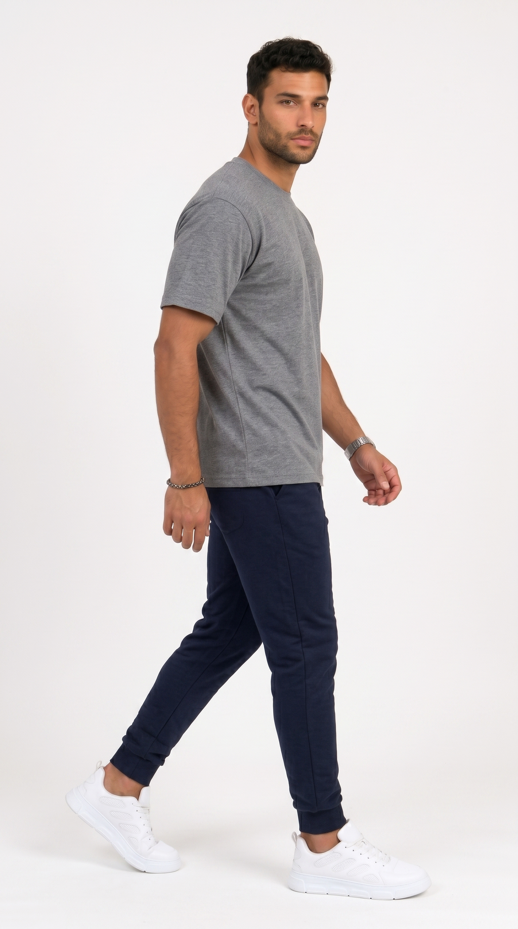 A man wearing a heather gray short-sleeve t-shirt, navy blue jogger pants, and white sneakers, captured in a side-profile walking pose against a clean white studio background, from Meleche Fashion USA or Meléche (short as (Mé))
