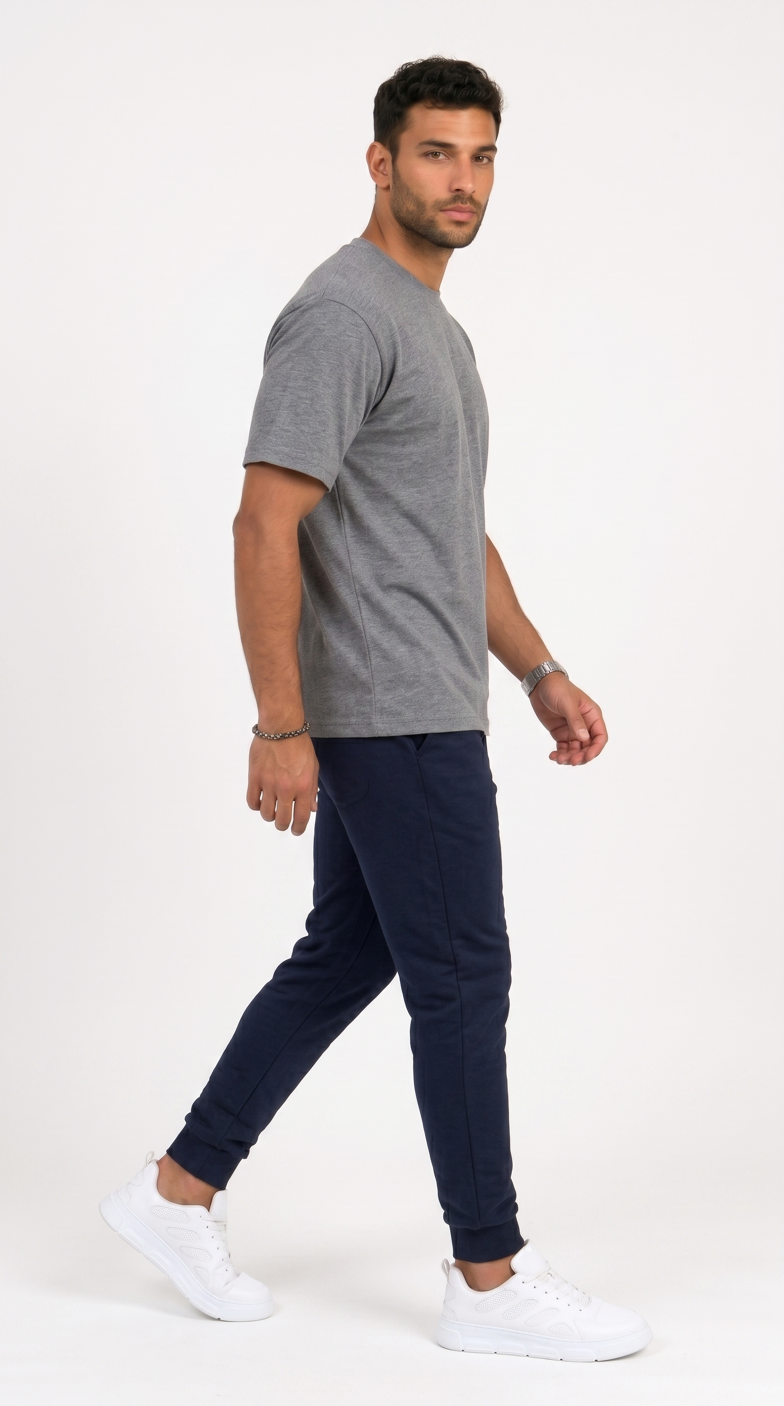 A man wearing a heather gray short-sleeve t-shirt, navy blue jogger pants, and white sneakers, captured in a side-profile walking pose against a clean white studio background, from Meleche Fashion USA or Meléche (short as (Mé))